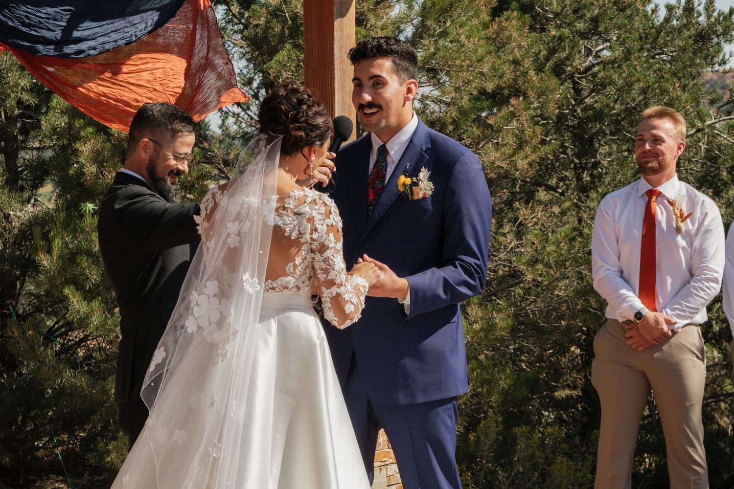 Wedding ceremony taking place under wooden pergola with scenic mountain backdrop.