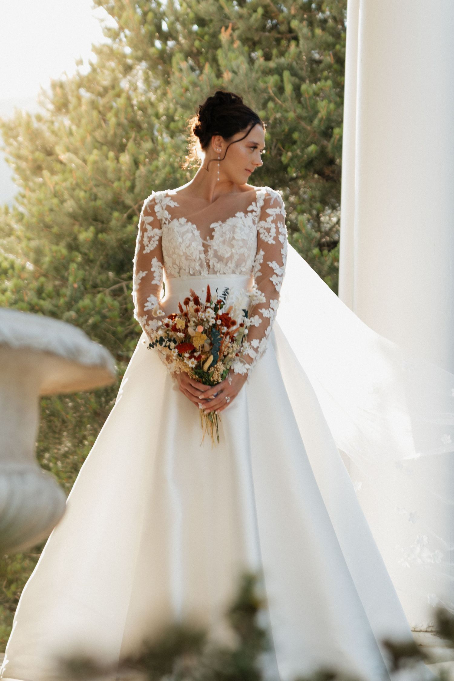 An elegant bridal portrait showcasing a long-sleeve lace wedding gown and autumn bouquet.