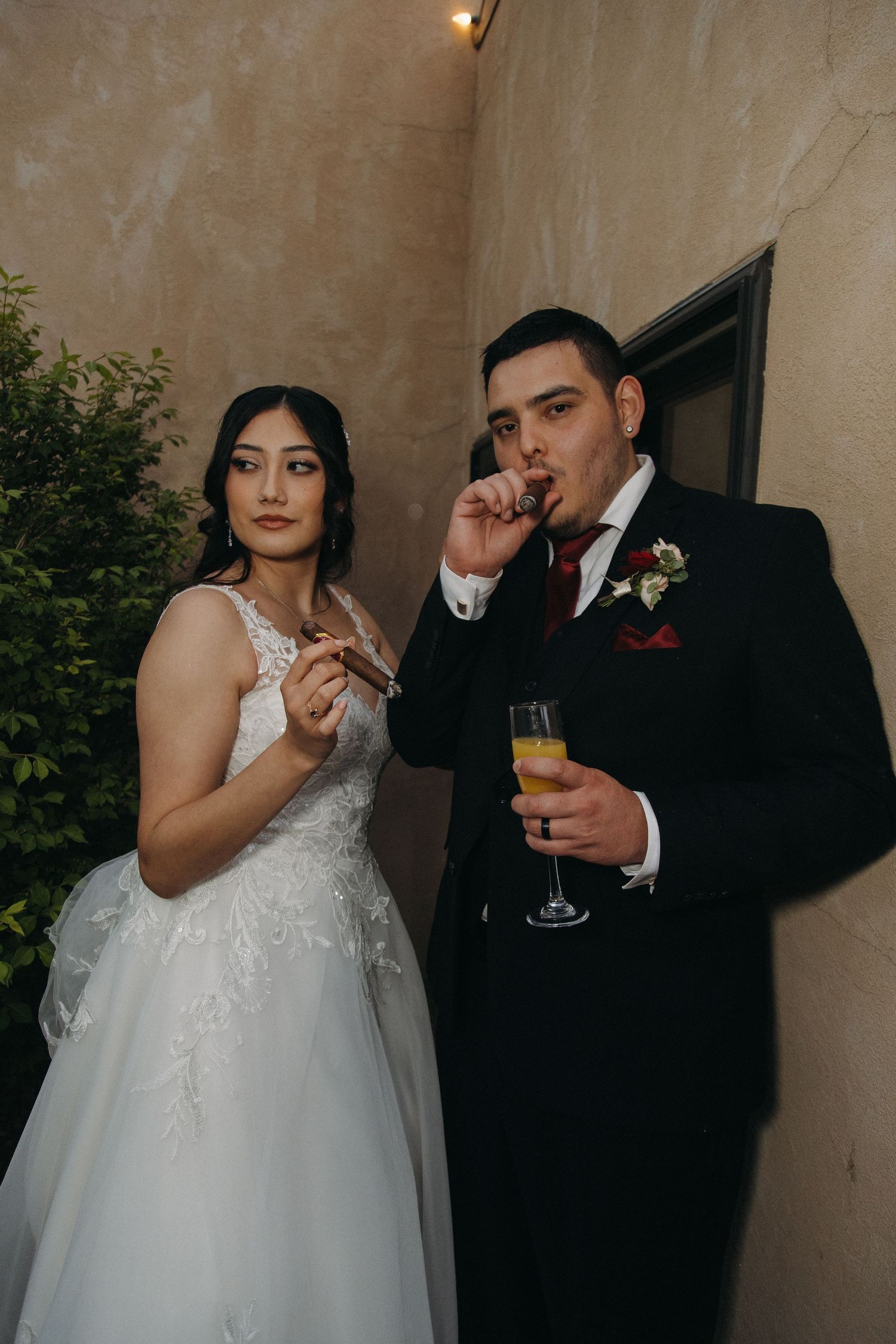 Bride and groom smoking cigars while groom holds champagne glass at wedding reception.