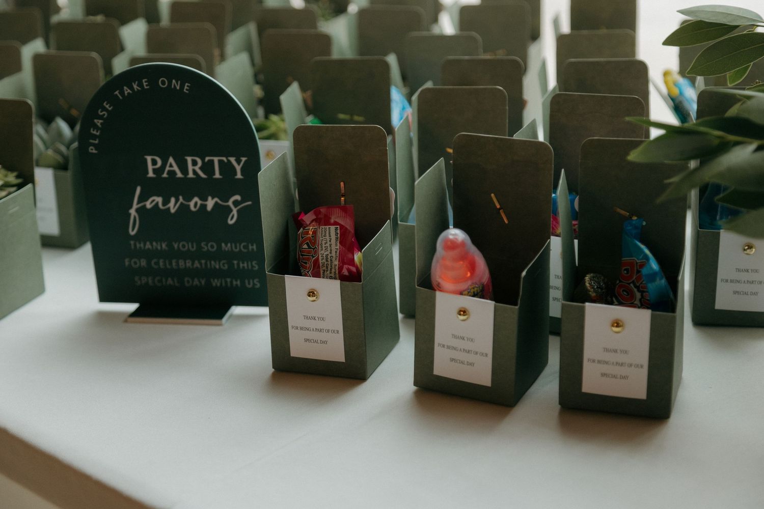 Green party favor boxes with colorful treats arranged on a white table at a wedding reception.
