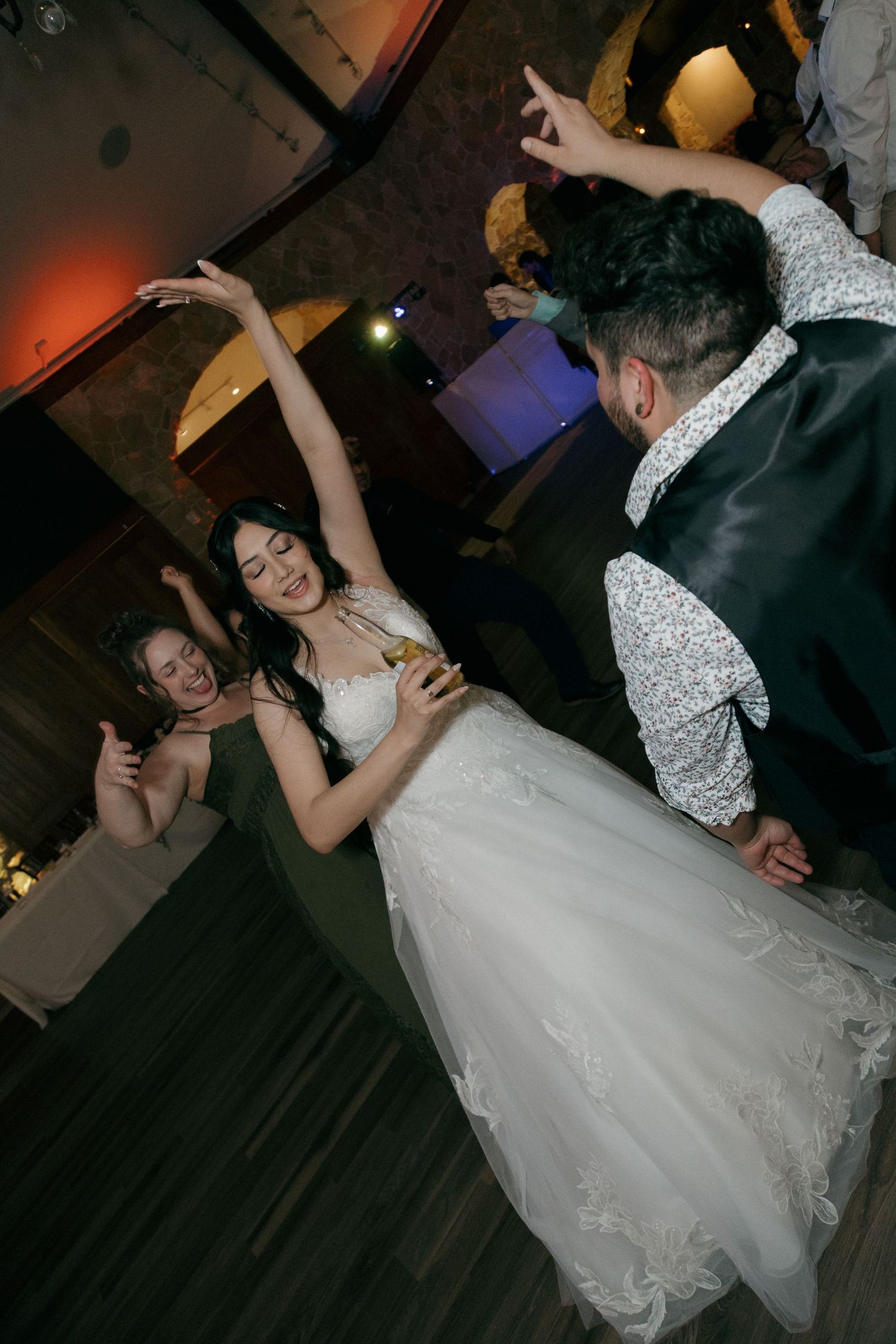 Bride in white gown dancing joyfully with guests at a lively wedding reception.