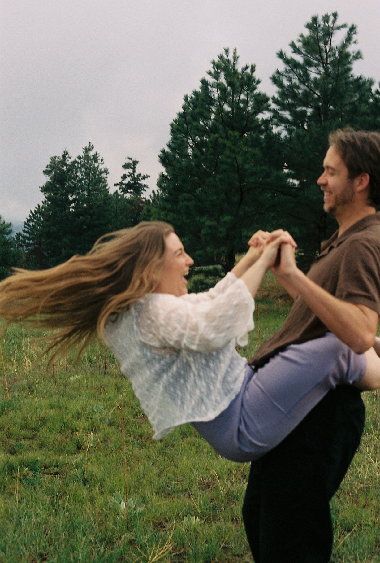 Joyful couple dancing and spinning together in a green meadow, woman's hair flowing in the wind.