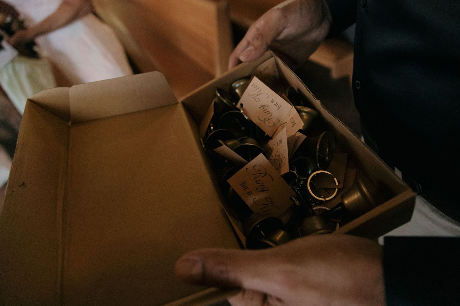 Hands holding an open box filled with wedding rings and small gift tags at a wedding.