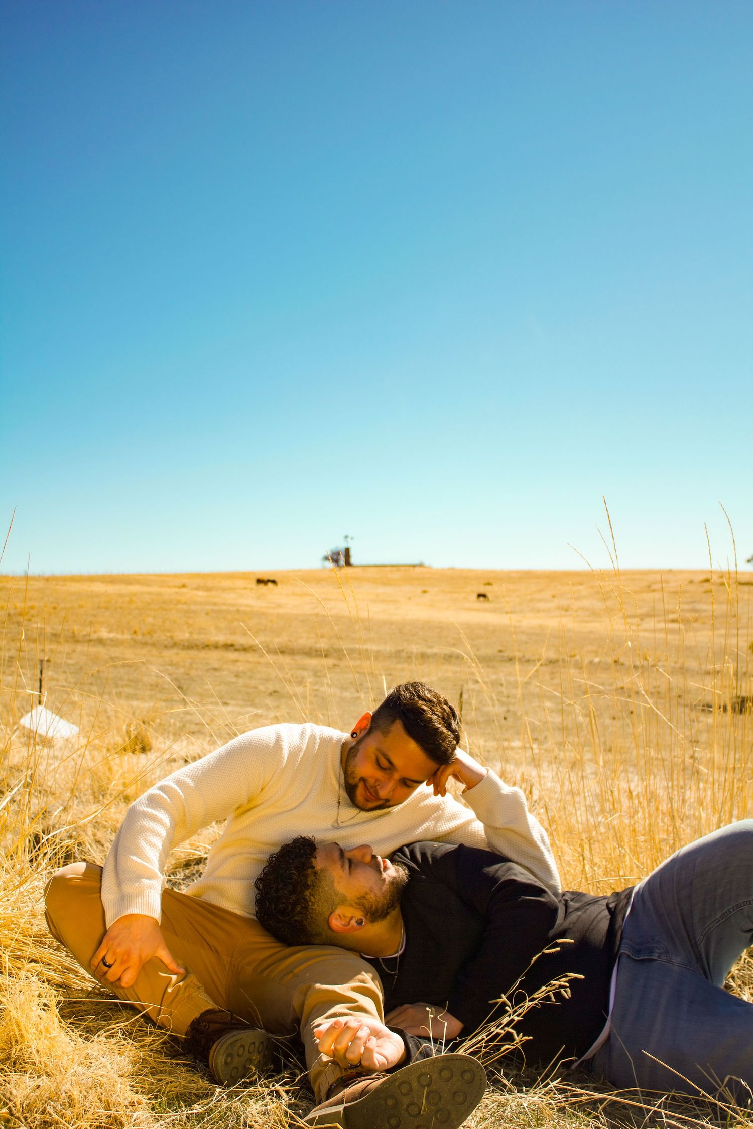 Two people lying together in golden grass under bright blue sky.
