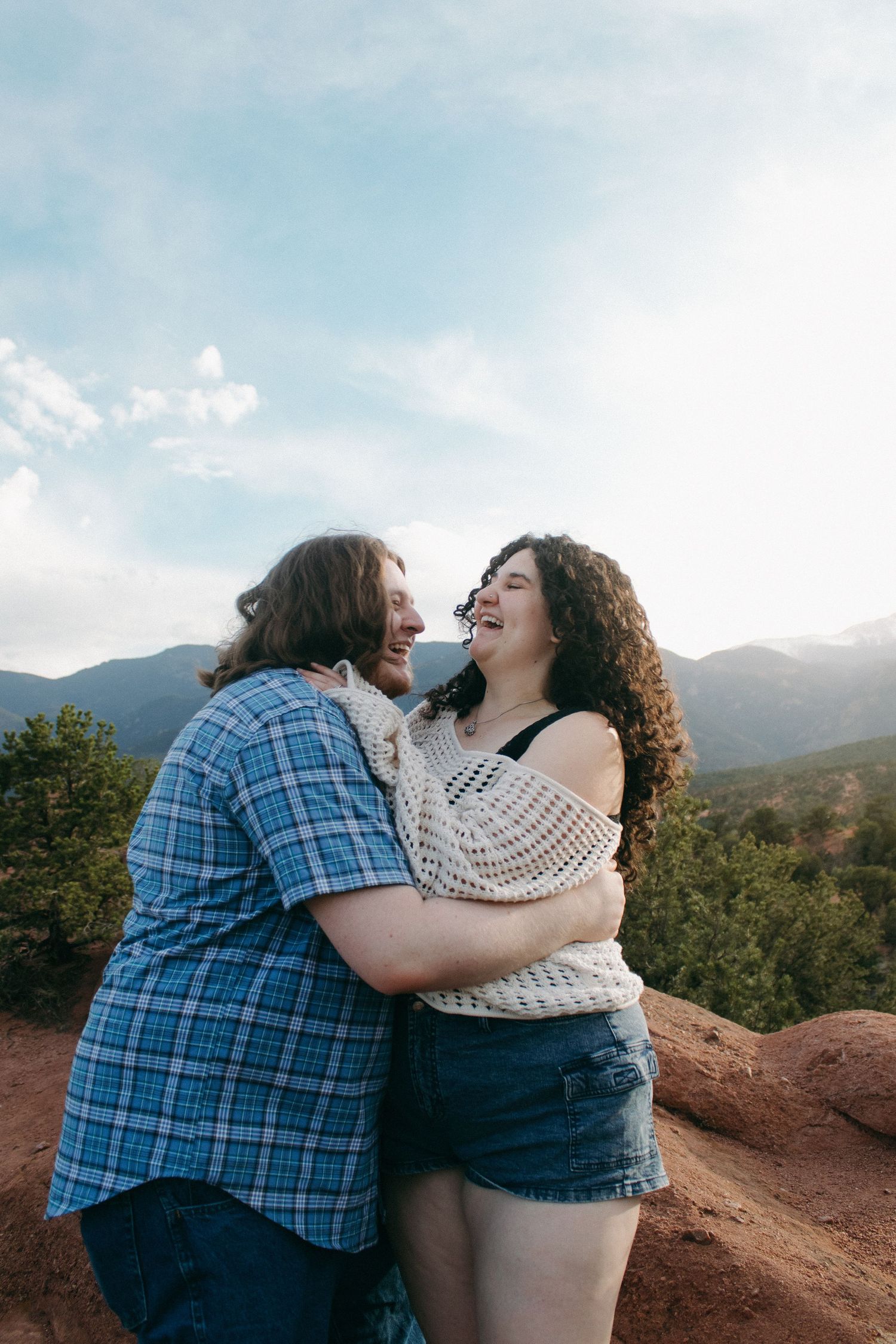 A couple sharing a joyful moment on red rocks with mountains and blue sky in the background.