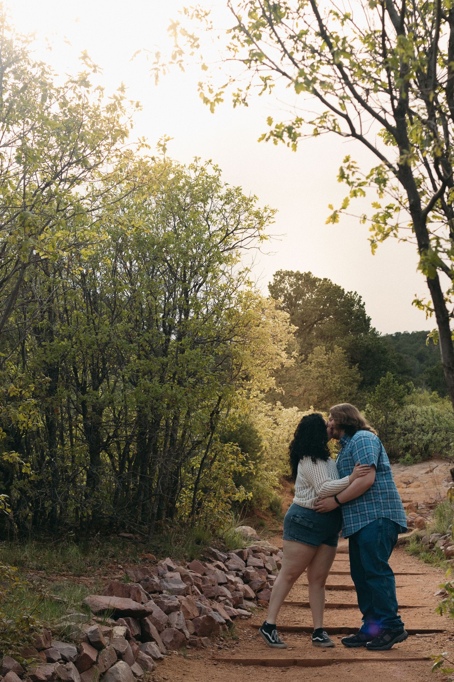 Couple embracing on a rocky hiking trail surrounded by green foliage.