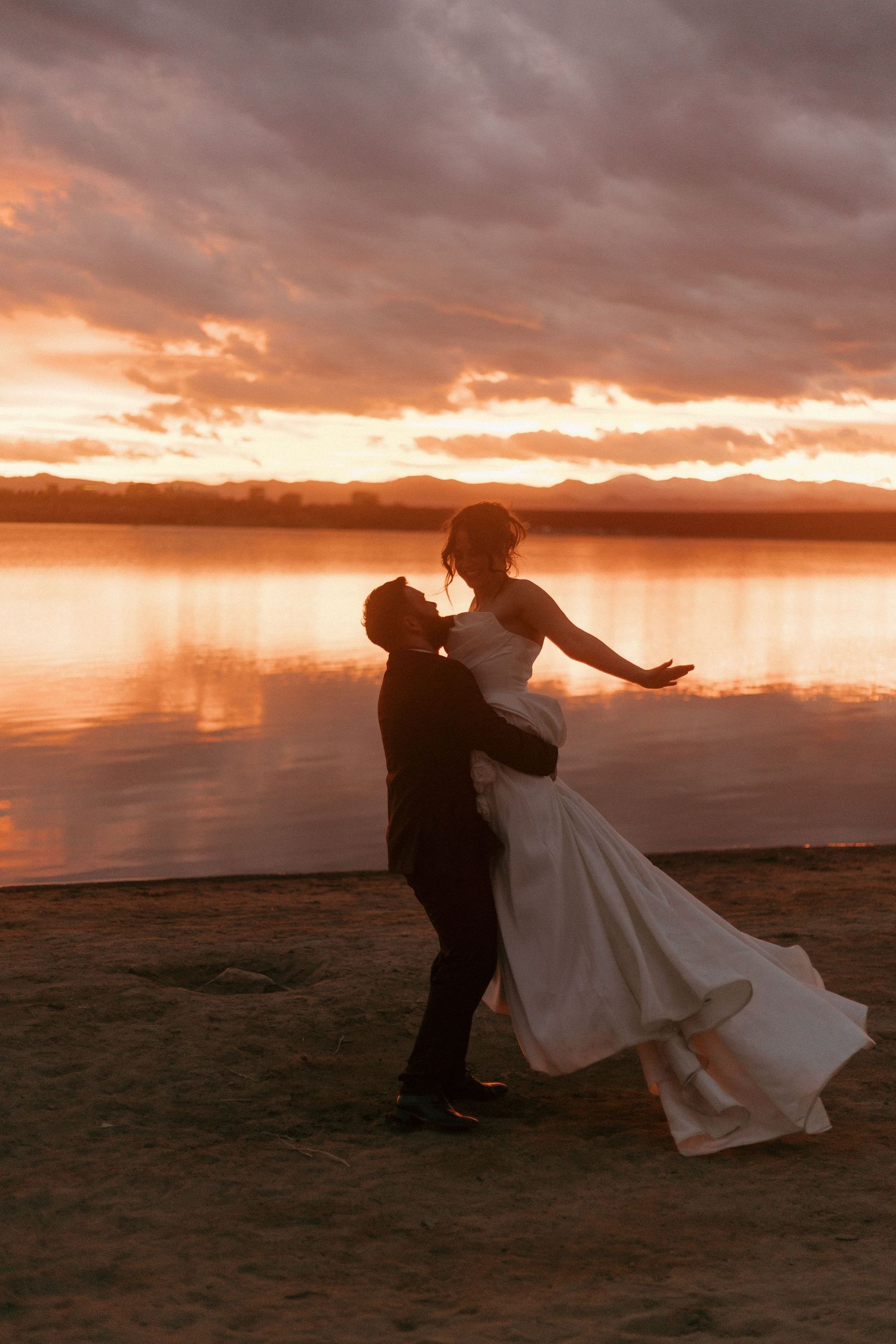 Silhouettes dance against a dramatic orange sunset sky on the shoreline.
