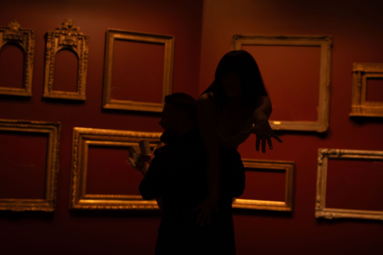 Dark interior gallery space with ornate gold frames on deep red walls.
