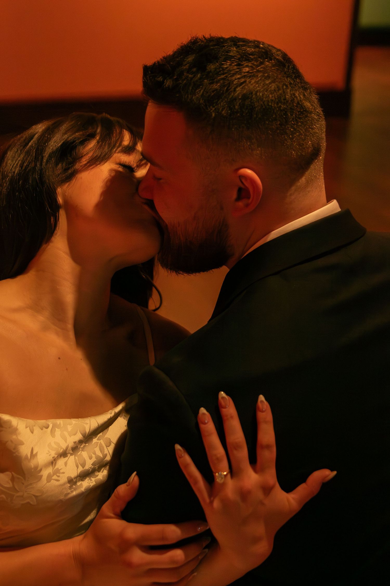 A couple shares passionate embraces in a dramatically lit gallery setting with orange walls.