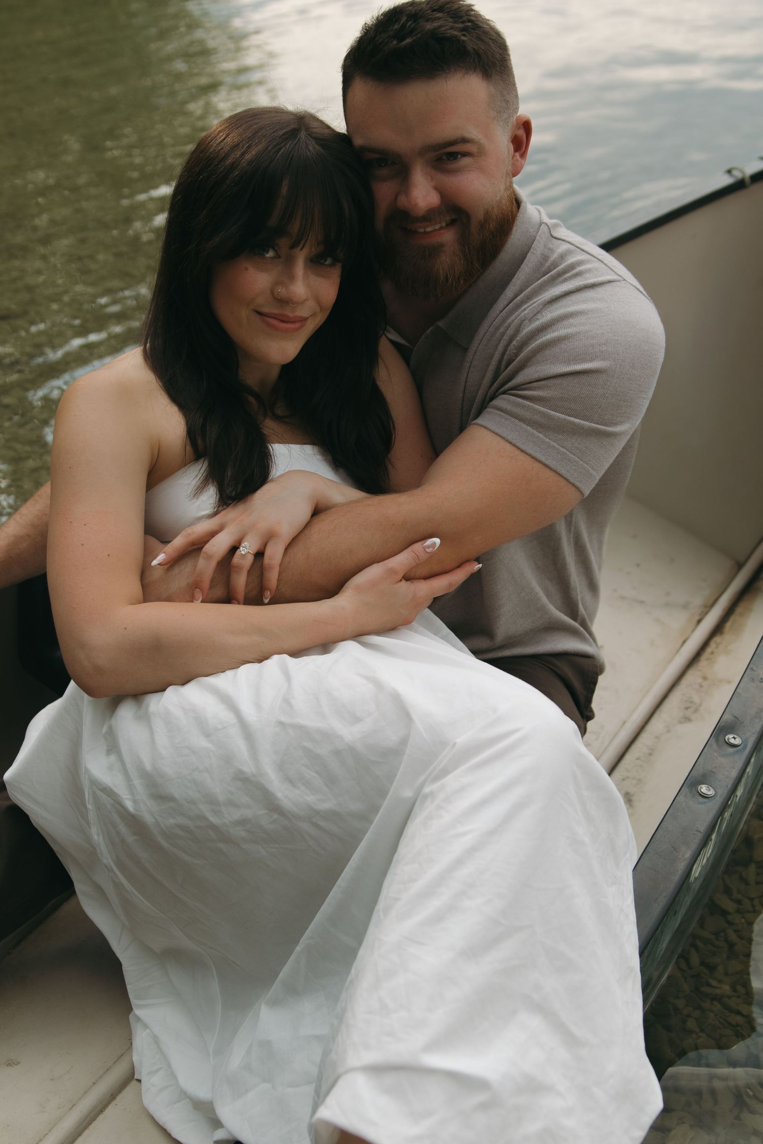 A romantic couple shares intimate moments while sitting in a boat on the water.