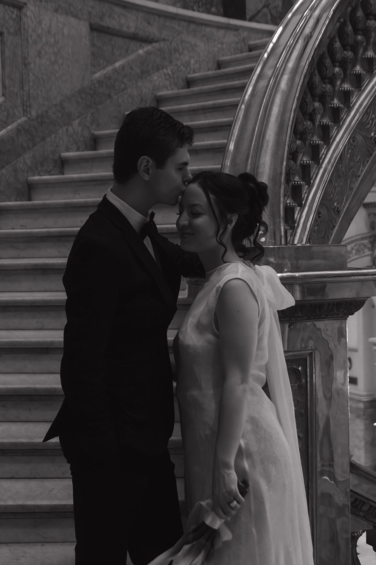 A romantic black and white wedding photo of a couple sharing an intimate moment on an elegant staircase.