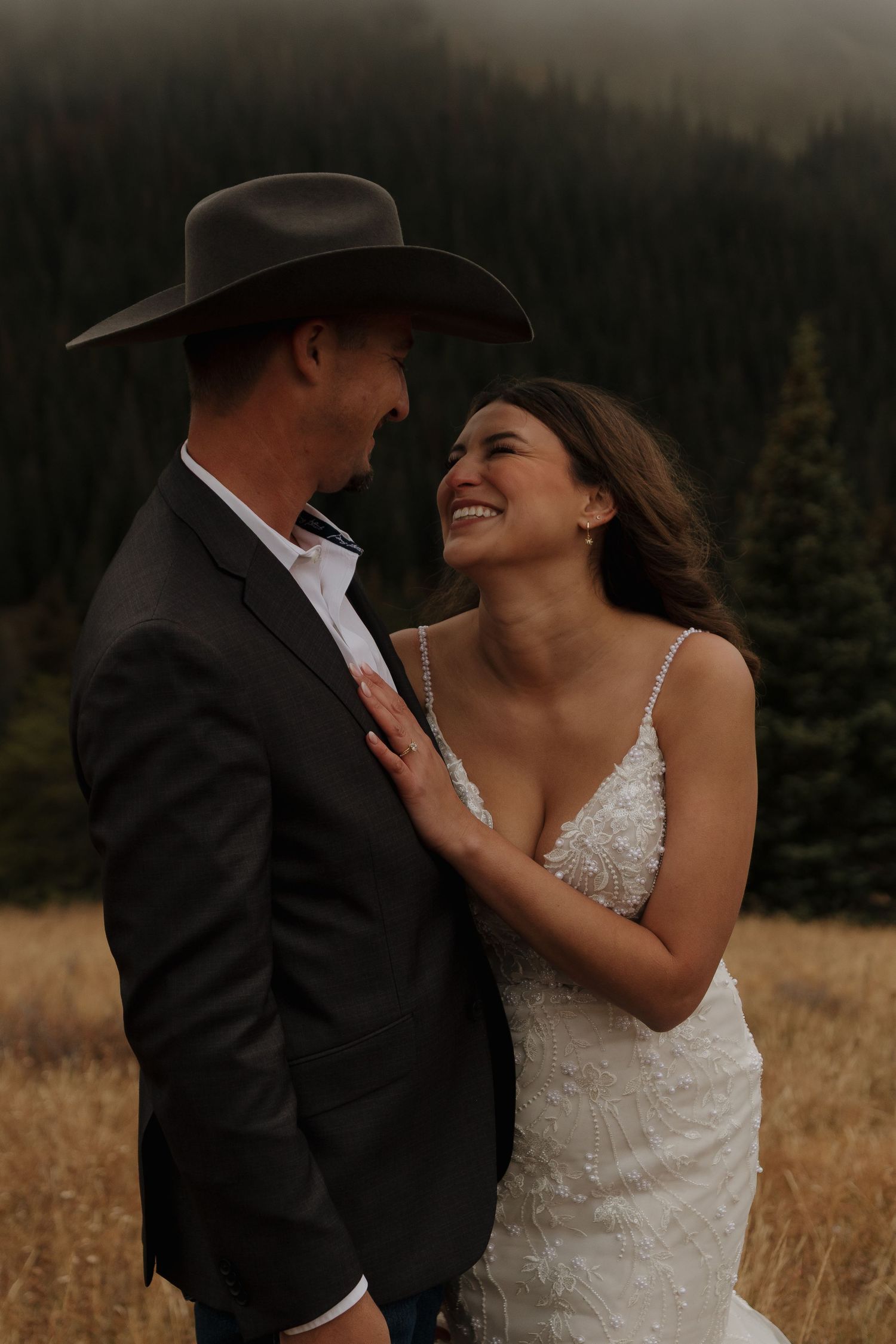 A romantic wedding portrait of a couple laughing together in a mountain field.