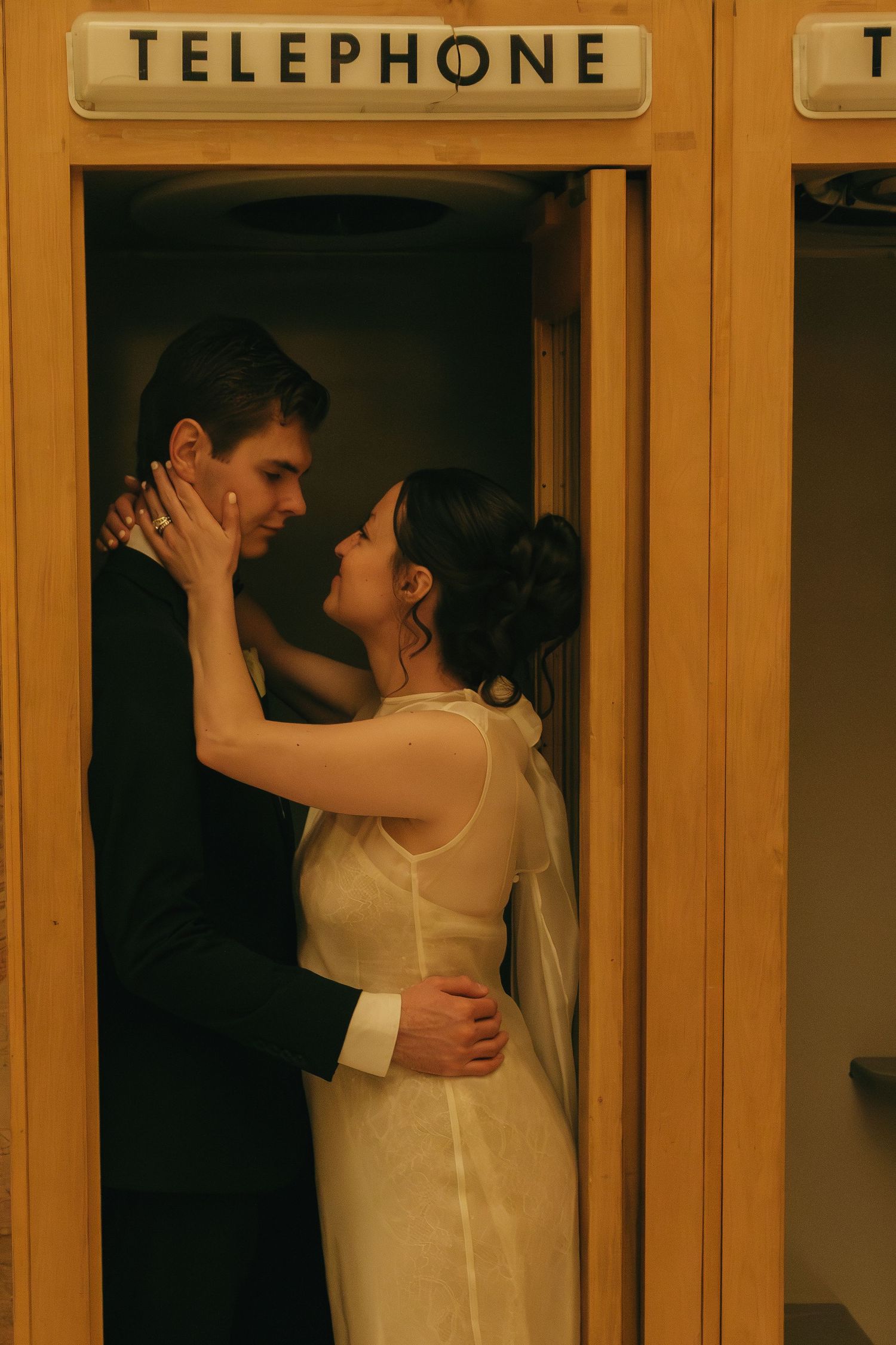 Newlyweds embrace in front of vintage telephone booths with warm golden lighting.