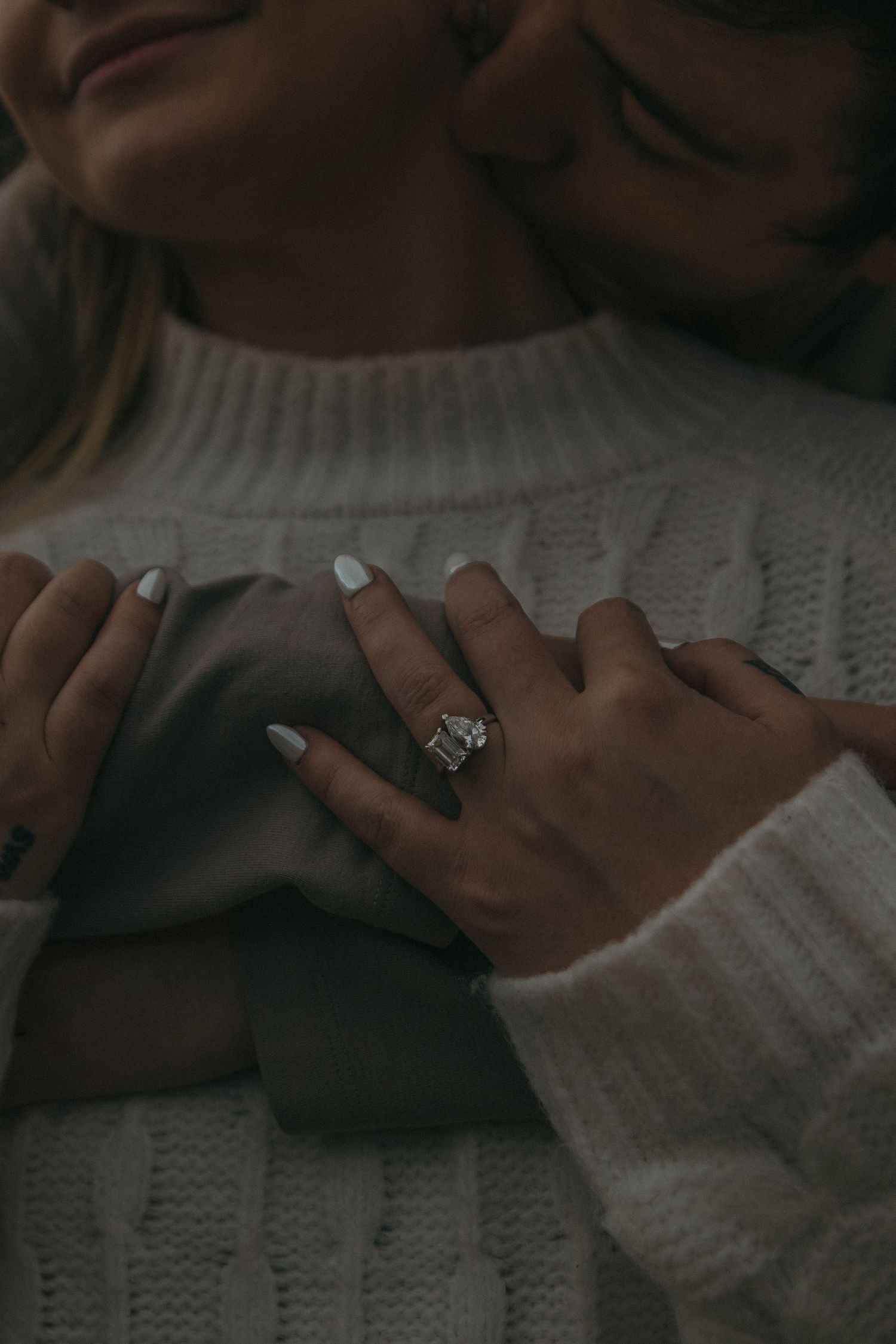 Close-up view of hands wearing a white knit sweater resting on a textured surface in moody lighting.