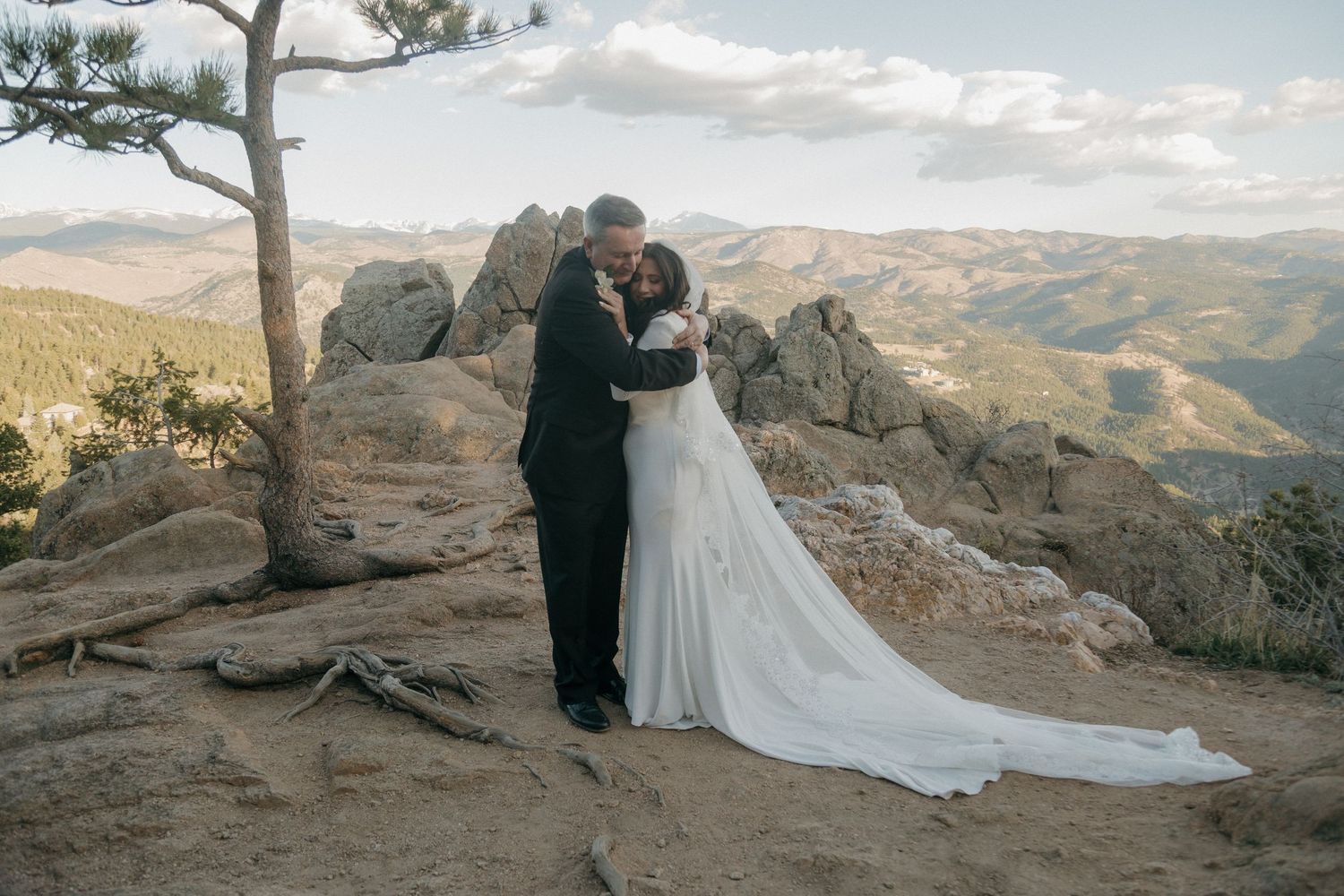 Bride and groom share romantic embrace on rocky mountain summit with sweeping Colorado landscape.