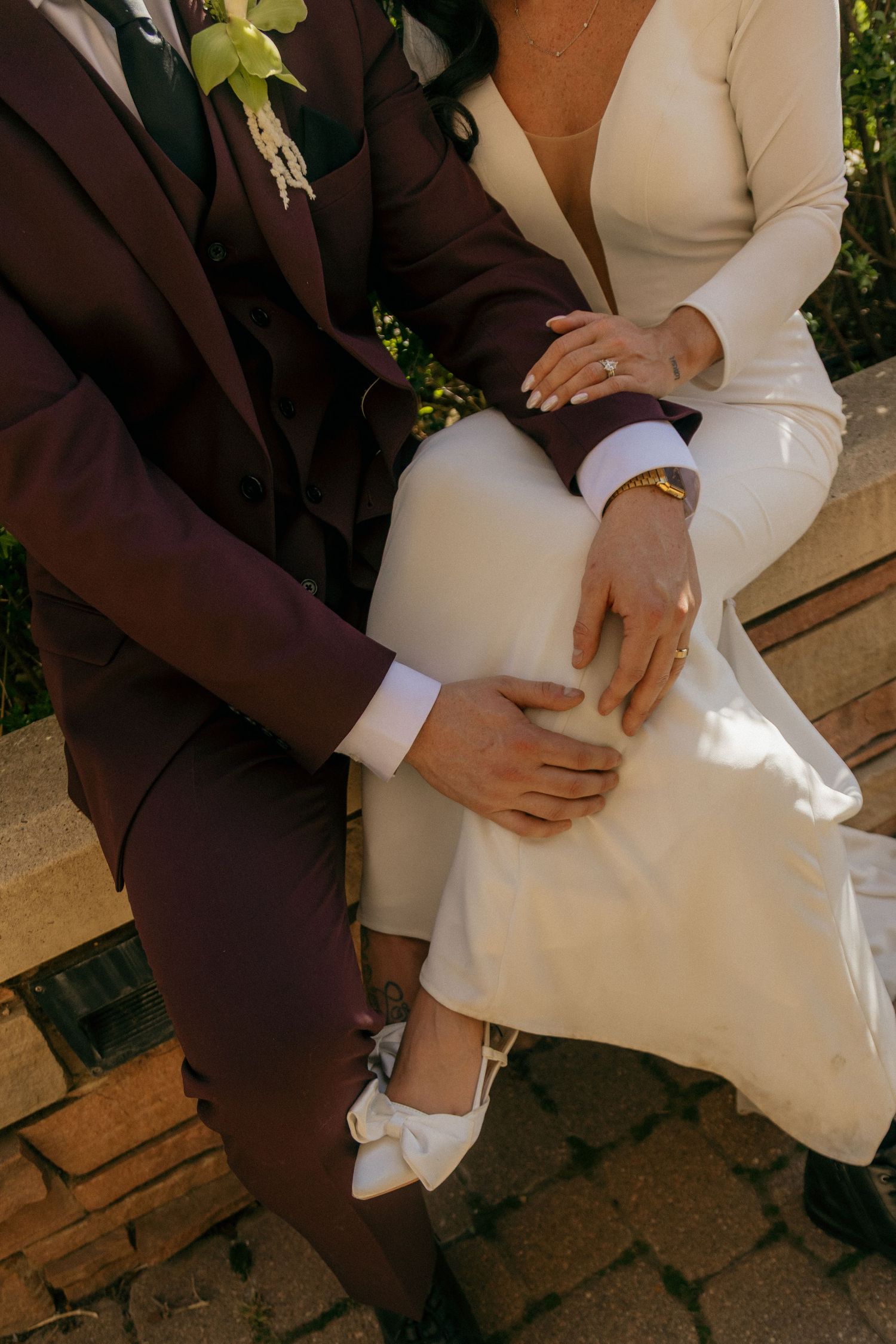 Close-up of bride and groom hands showing wedding rings while seated outdoors together.