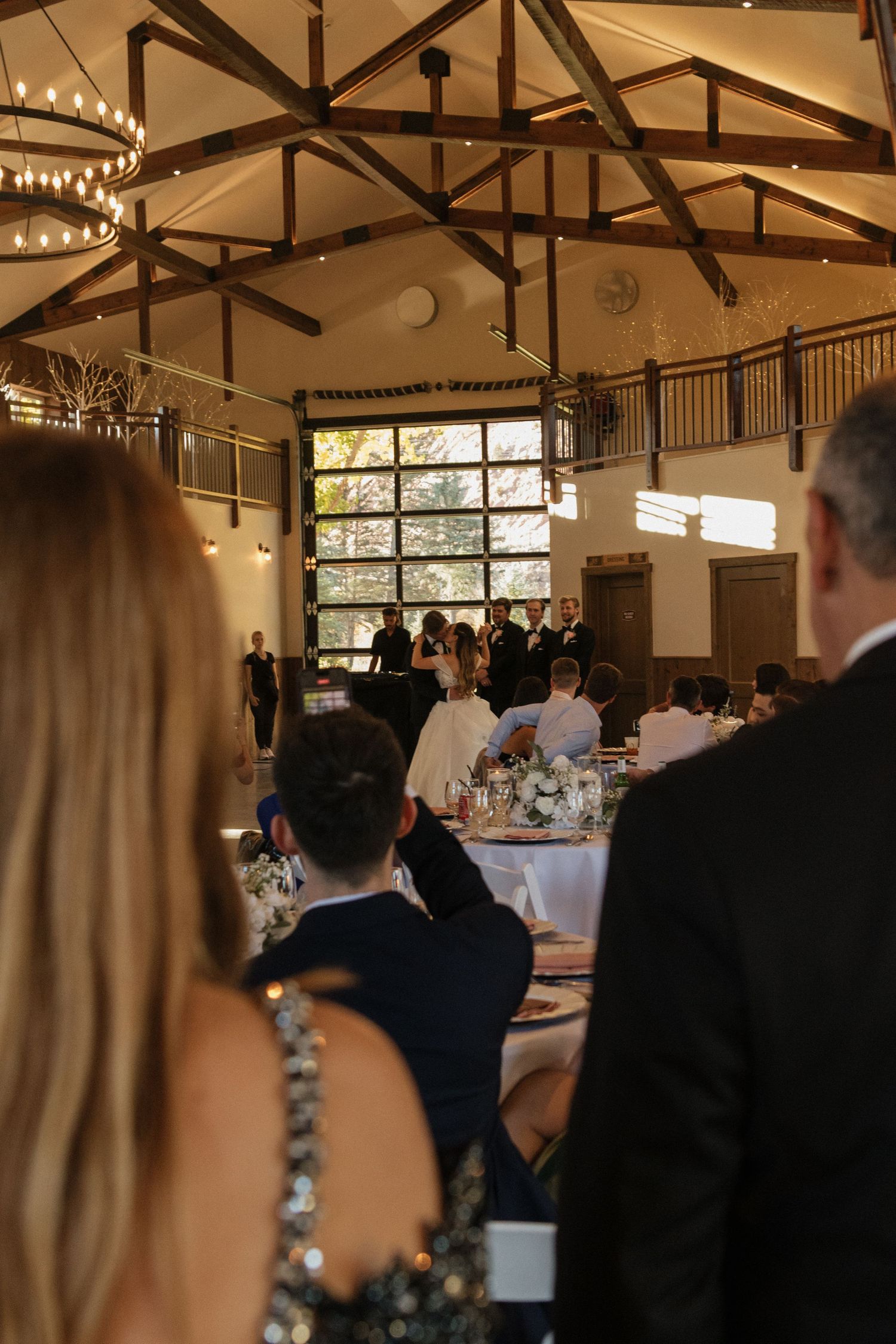 Wedding reception venue with exposed wooden beams, chandeliers, and large windows.