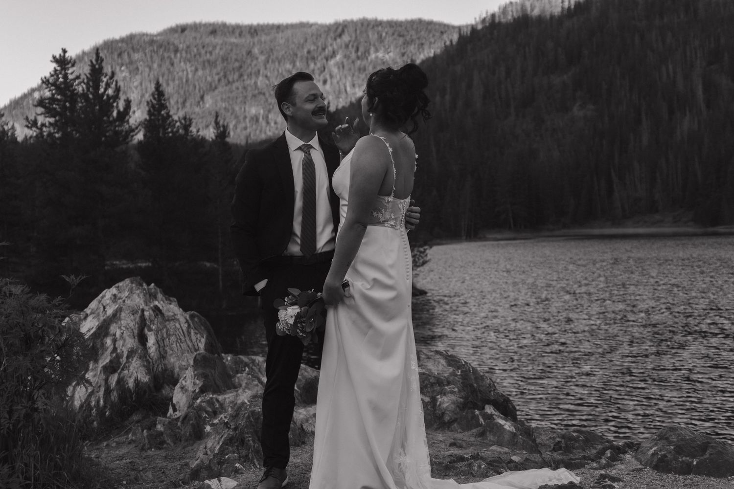 Black and white collage of romantic wedding moments by a lake with mountains and forest in the background.