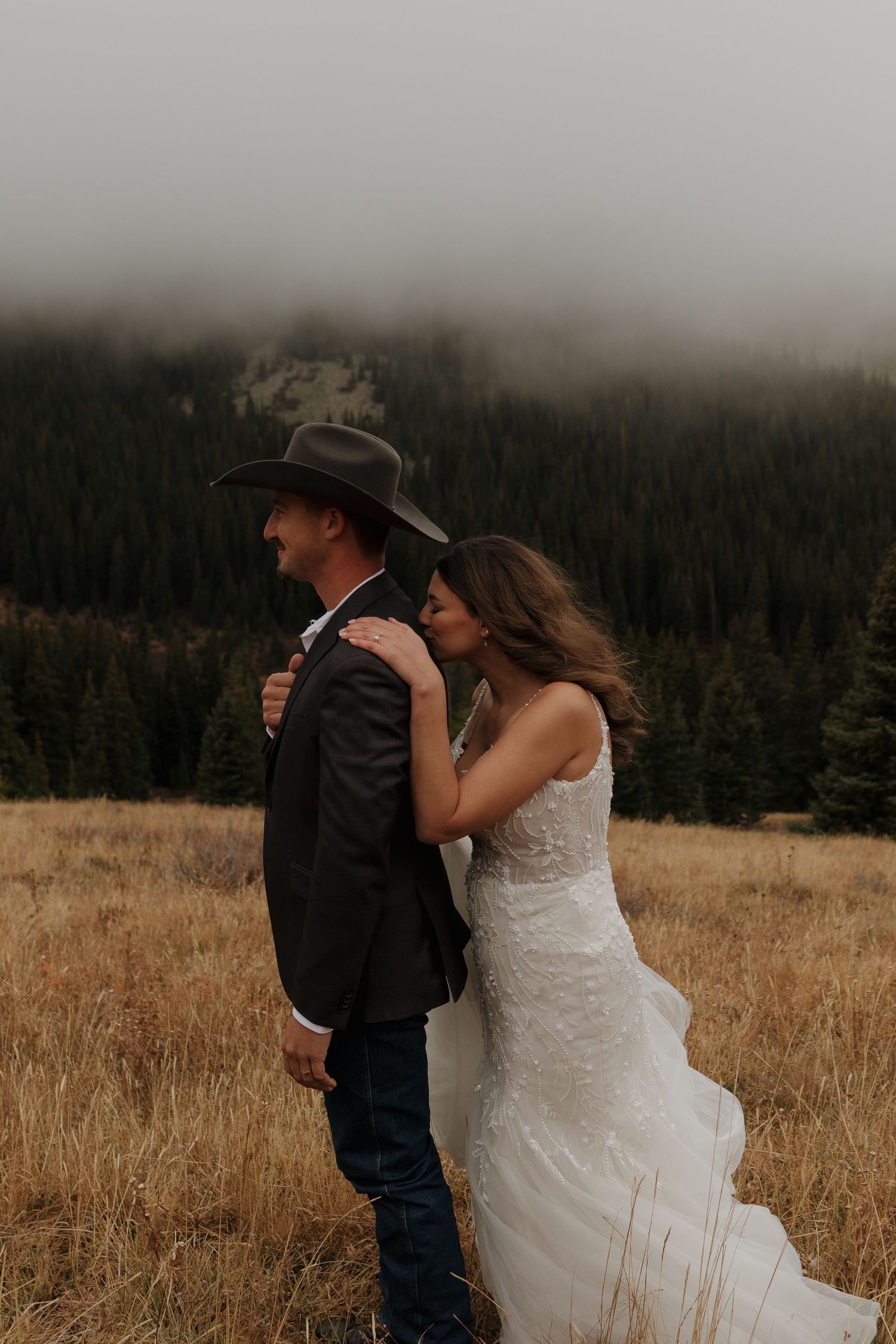A couple shares an intimate moment in a misty mountain meadow during their wedding.