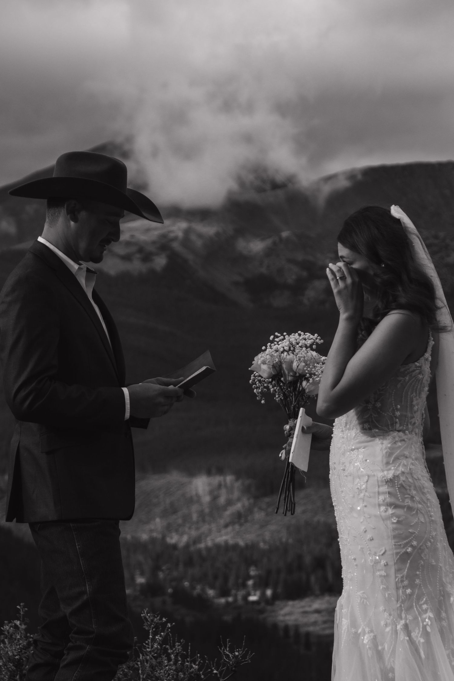 An emotional wedding ceremony moment captured in black and white against mountain scenery.