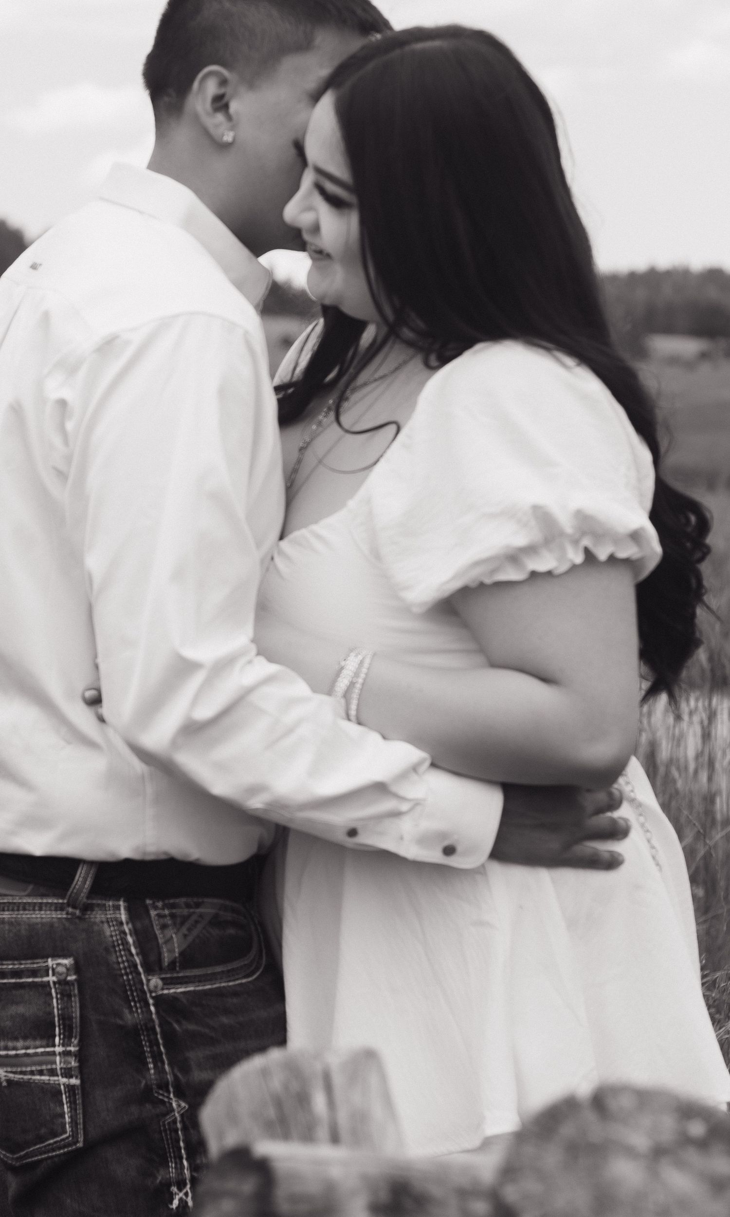 Intimate black and white portrait of couple in white clothing embracing in a field.