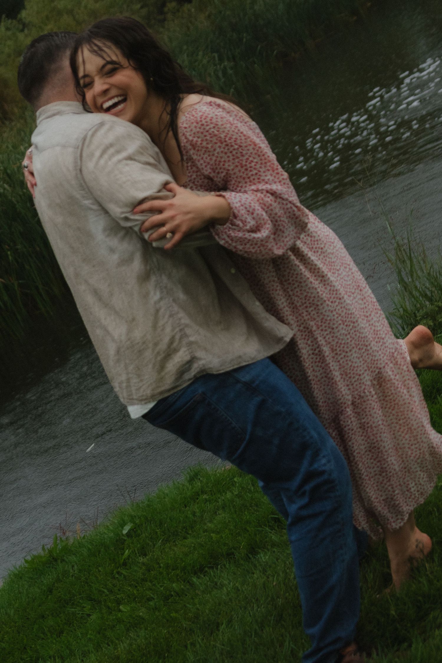 A joyful couple shares playful moments by a lake, with the woman wearing a floral dress.