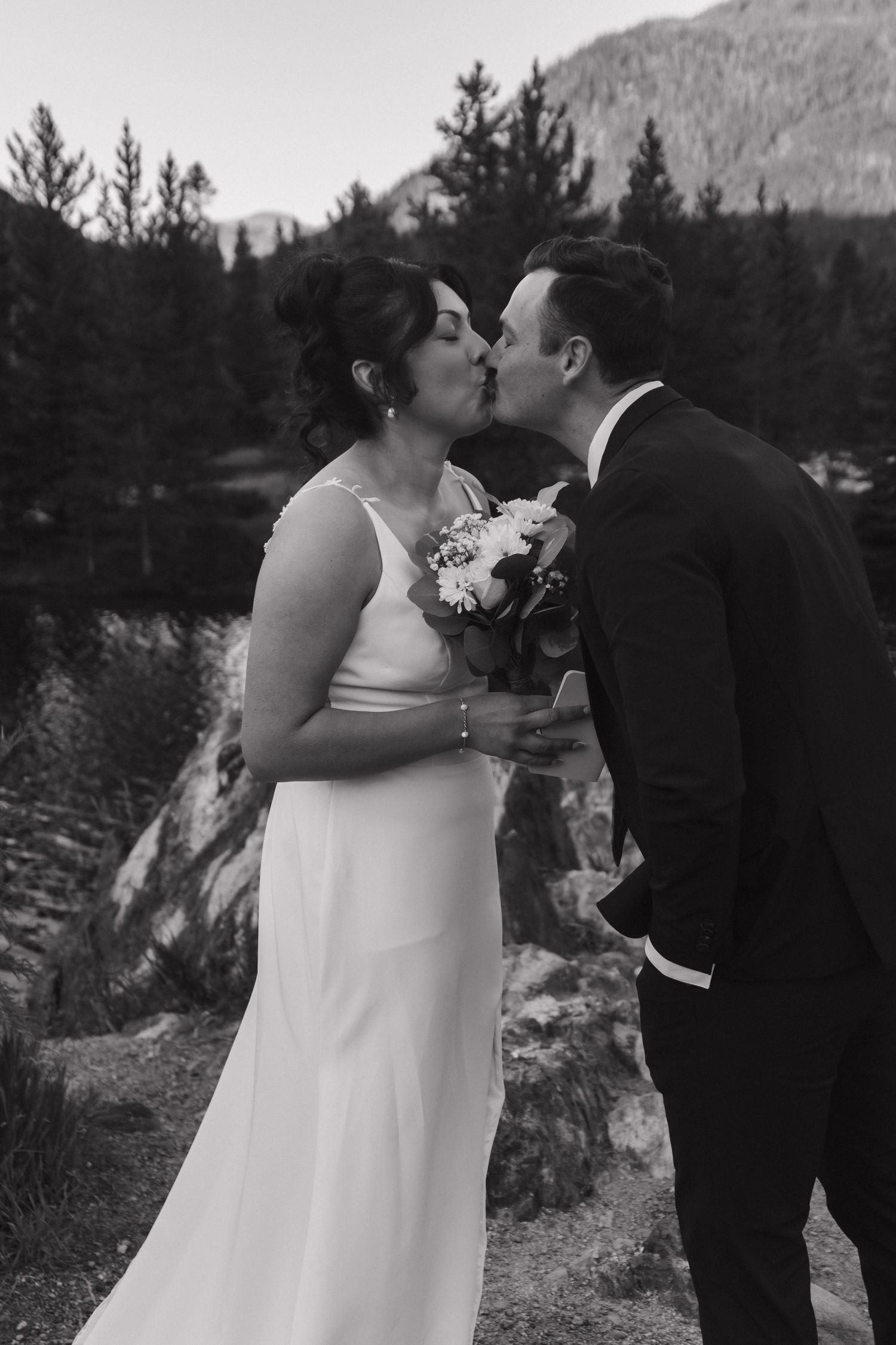 Wedding ceremony moment at sunset with mountain landscape and evergreen trees in the background.