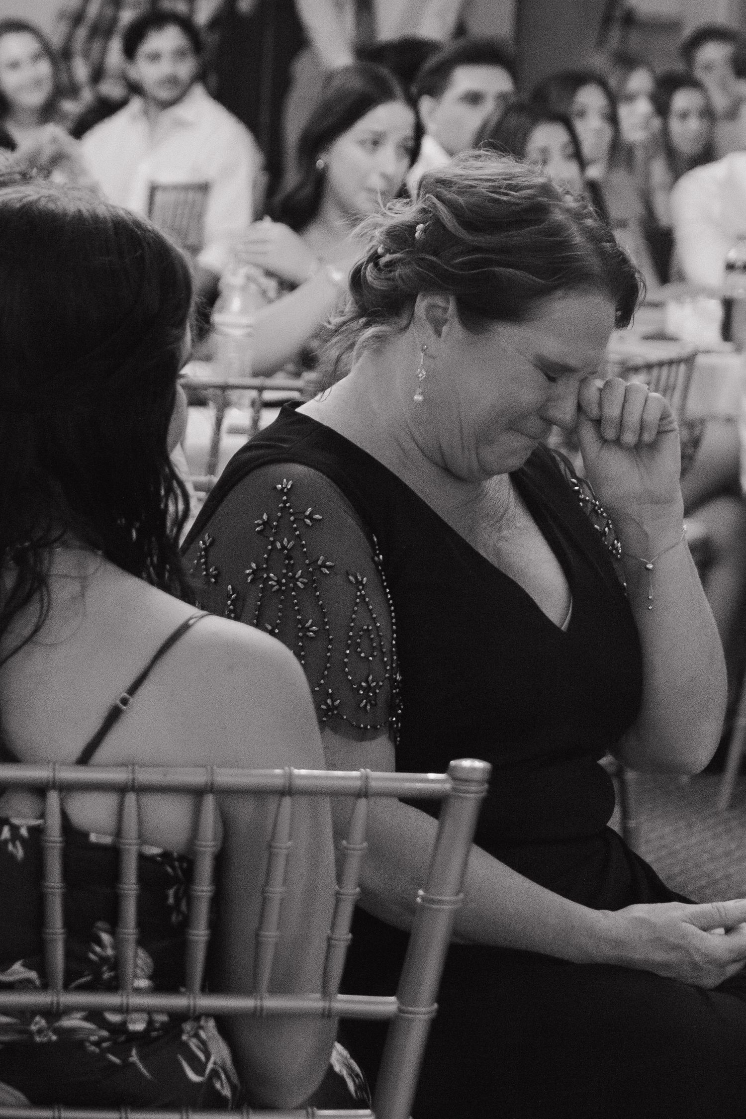 Wedding guests in formal attire seated at tables during an emotional moment of the reception.