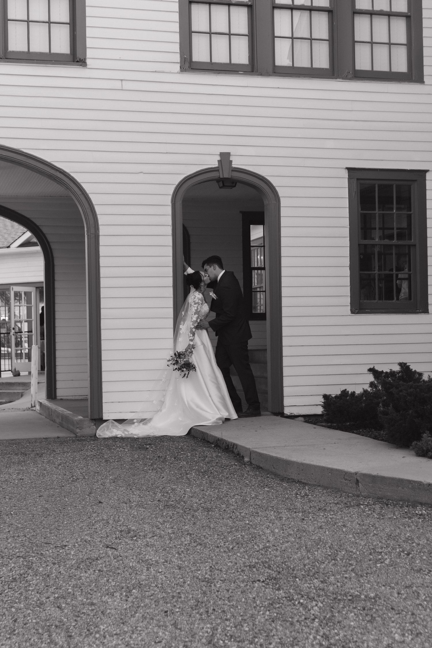 A classic black and white wedding portrait taken under the arches of a white colonial building.