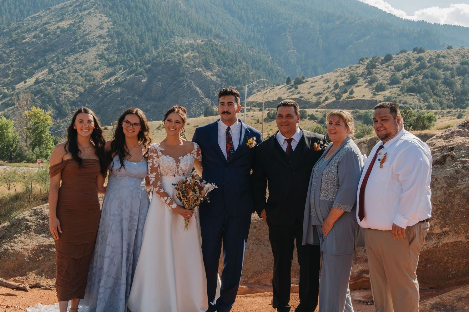 Wedding party group photos with mountain landscape backdrop on sunny day.