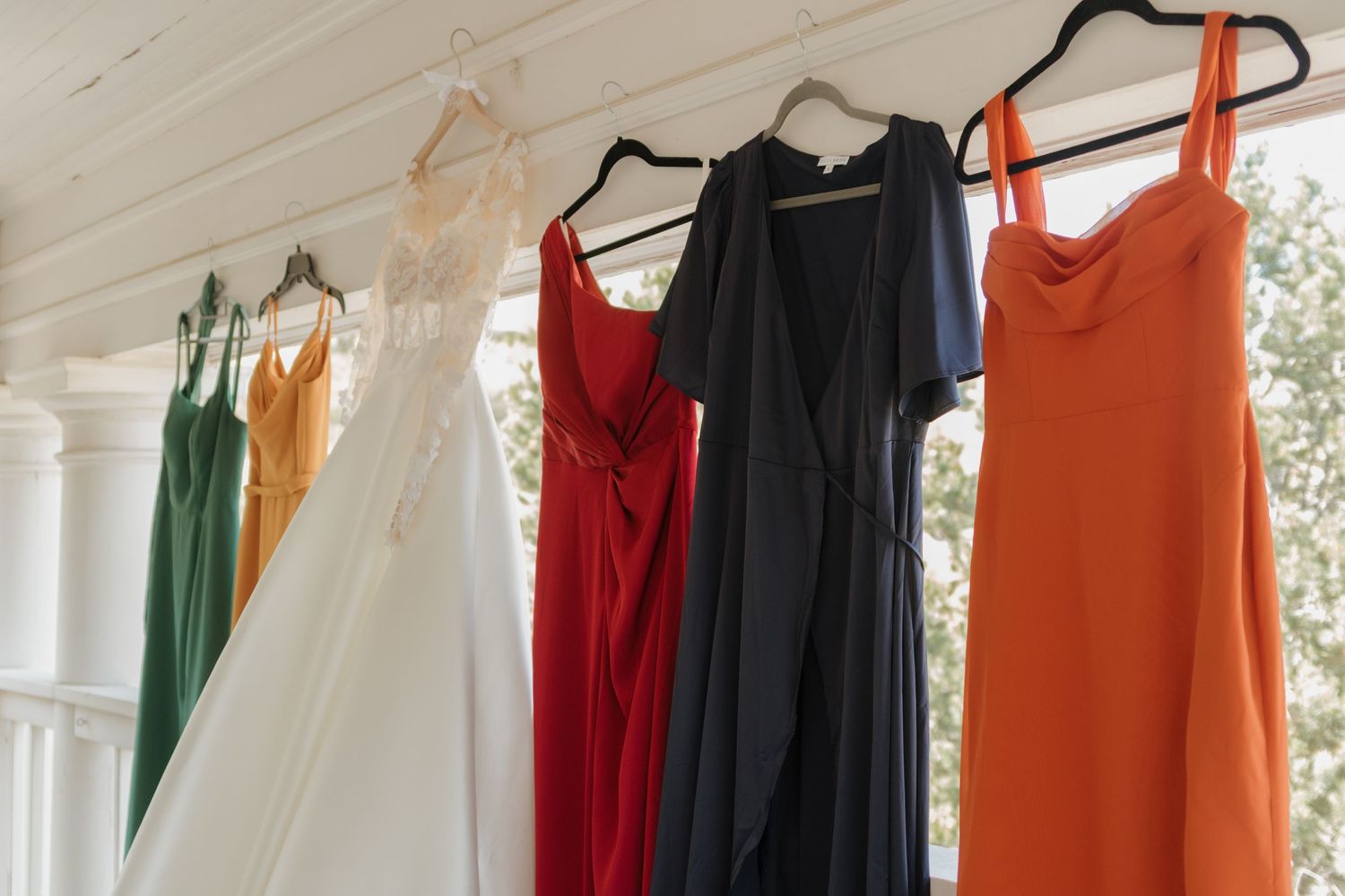 Colorful dresses and garments hanging on white hangers against a white wall in a boutique display.