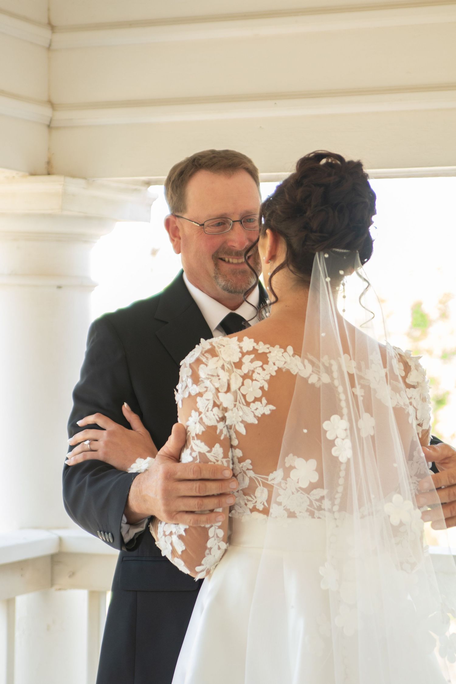 Bride in lace veil shares tender first look moment during wedding preparations.