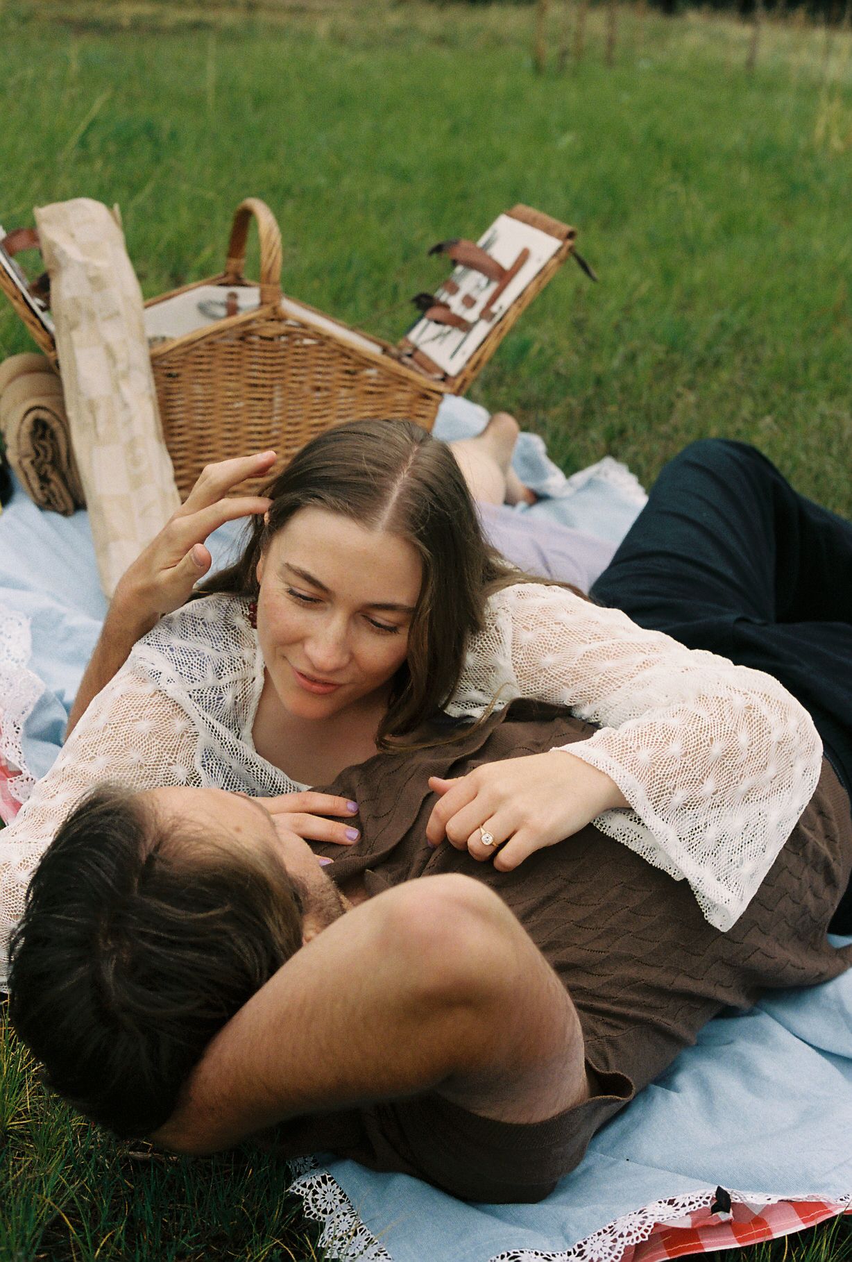 Couple lying together on a picnic blanket, sharing a tender moment near a wicker basket.