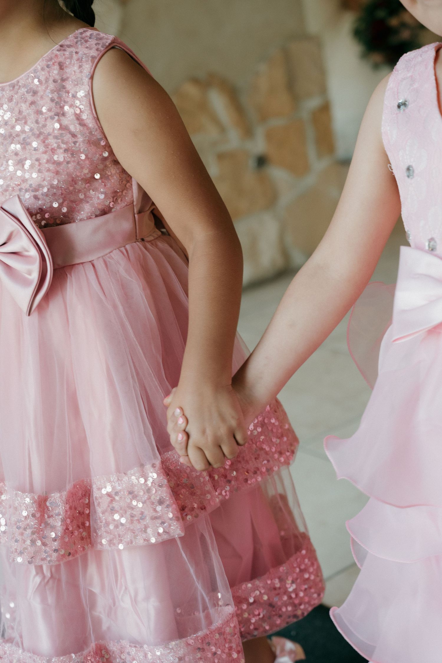 Two young flower girls in pink sequined dresses hold hands at elegant wedding ceremony.