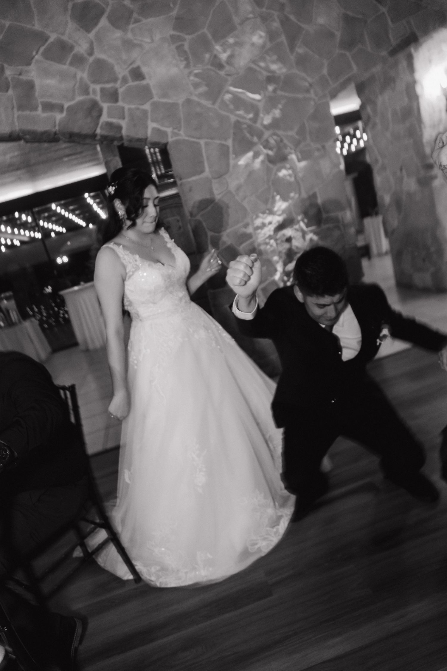 Bride and groom celebrate on the dance floor with a guest at their rustic stone wedding reception.