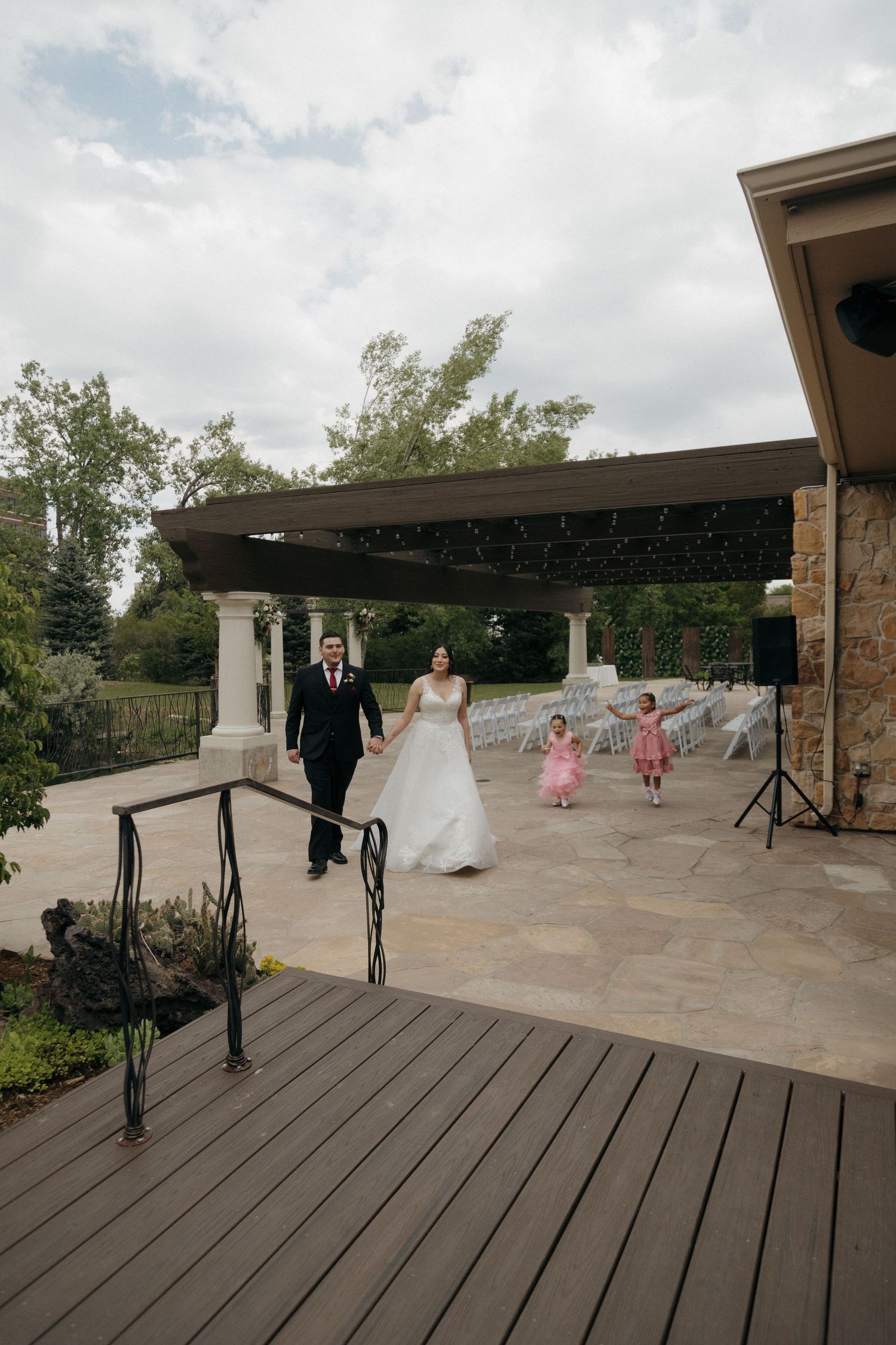Bride and groom walking with two flower girls in pink dresses at outdoor wedding venue.