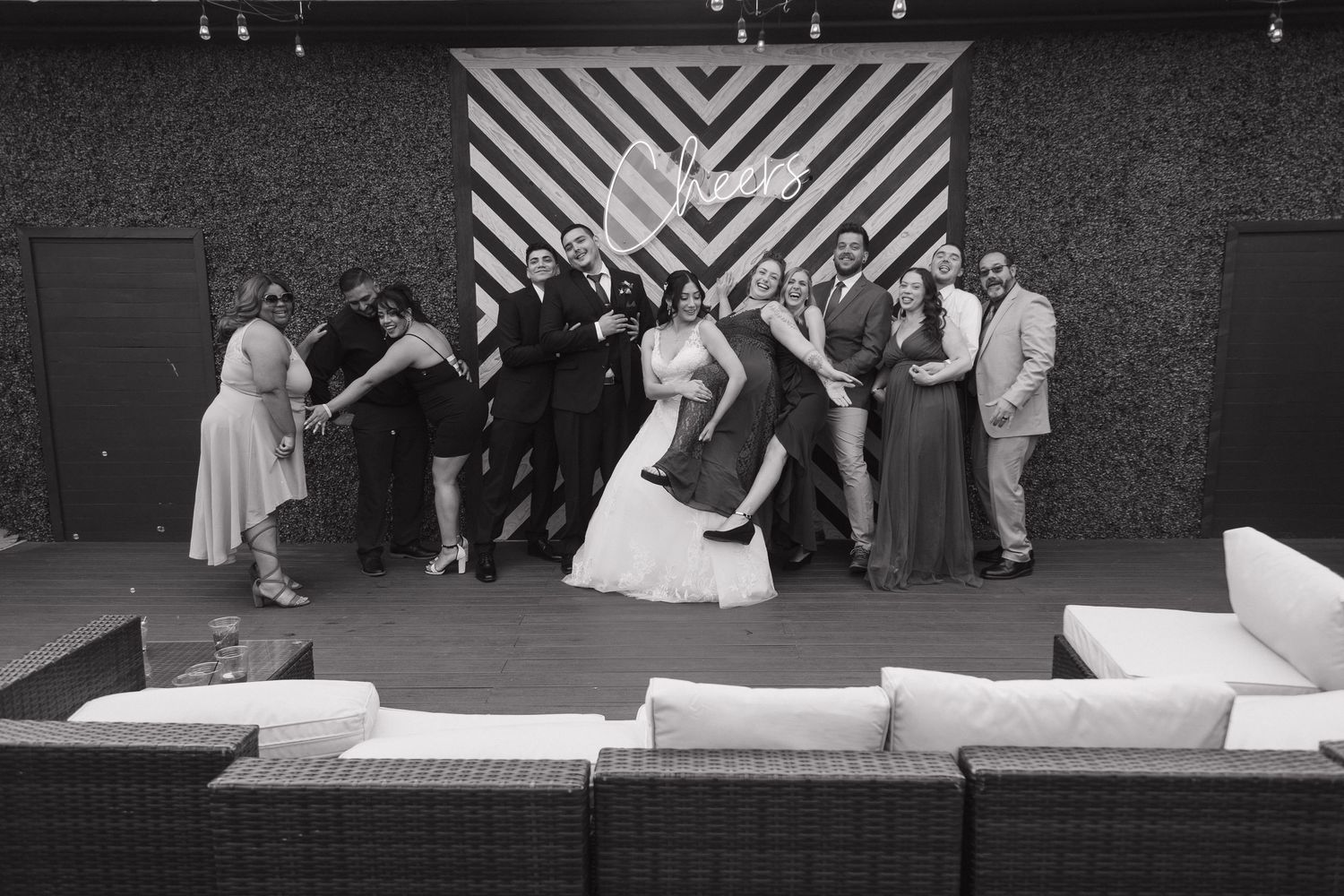 Black and white photo of wedding party posing playfully in front of striped backdrop at reception venue.