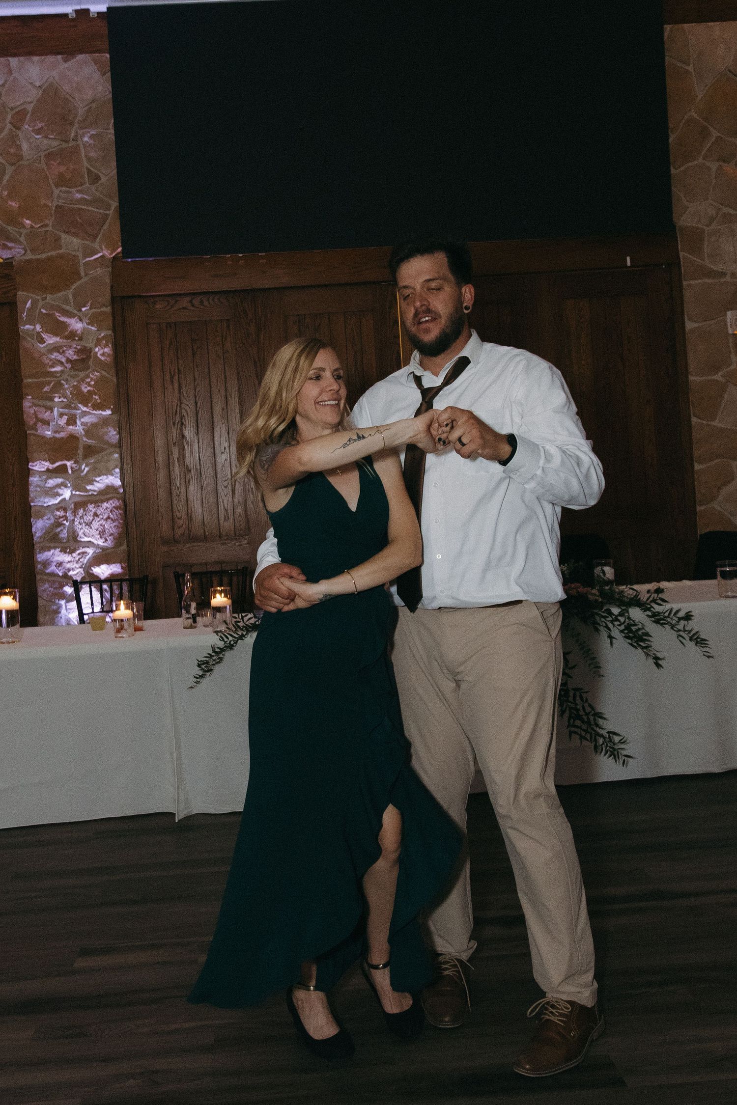 Couple shares a playful dance moment in elegant attire at a warmly lit wedding reception.