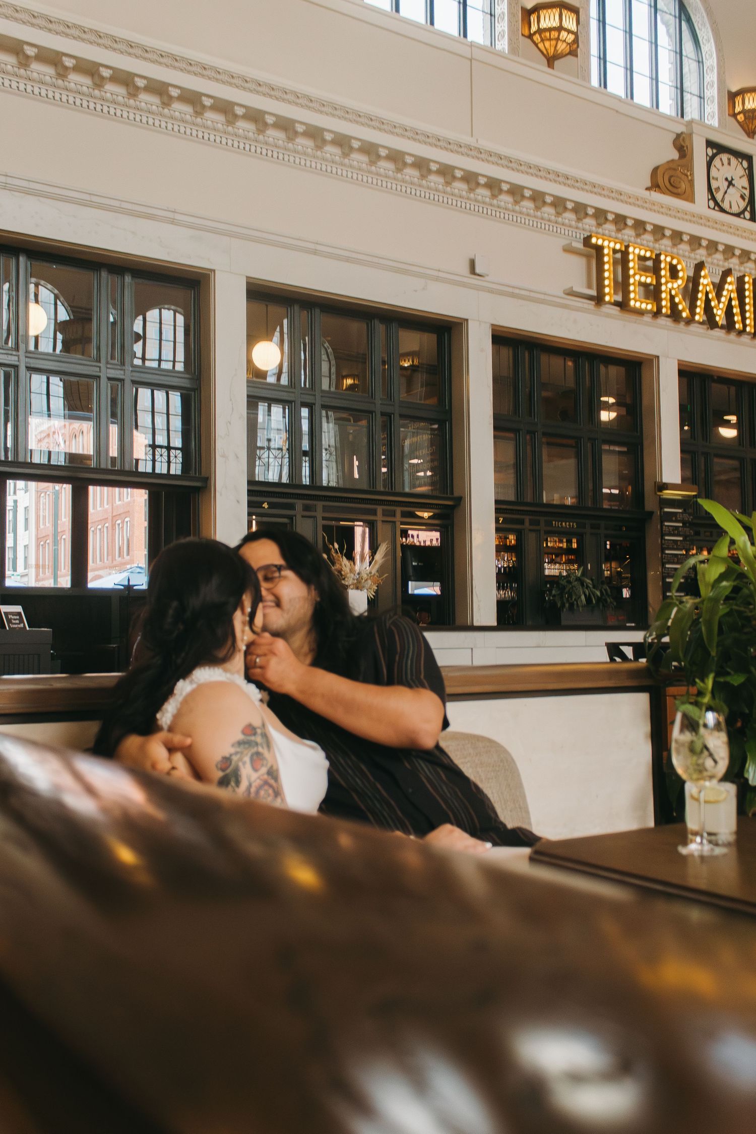 Couple shares intimate moments in historic train station restaurant with vintage lighting.
