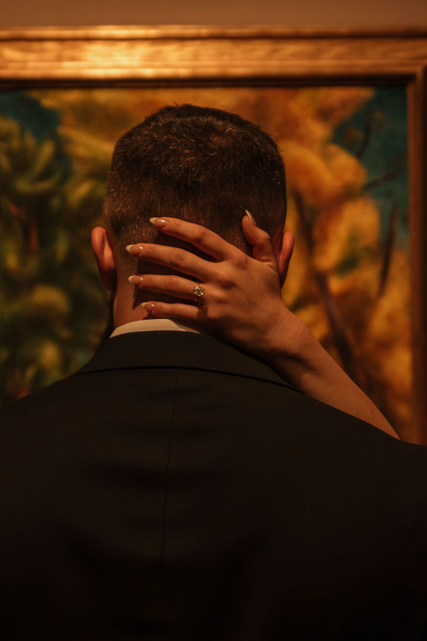 Close-up of hands with a wedding ring resting on the back of someone wearing a black suit.
