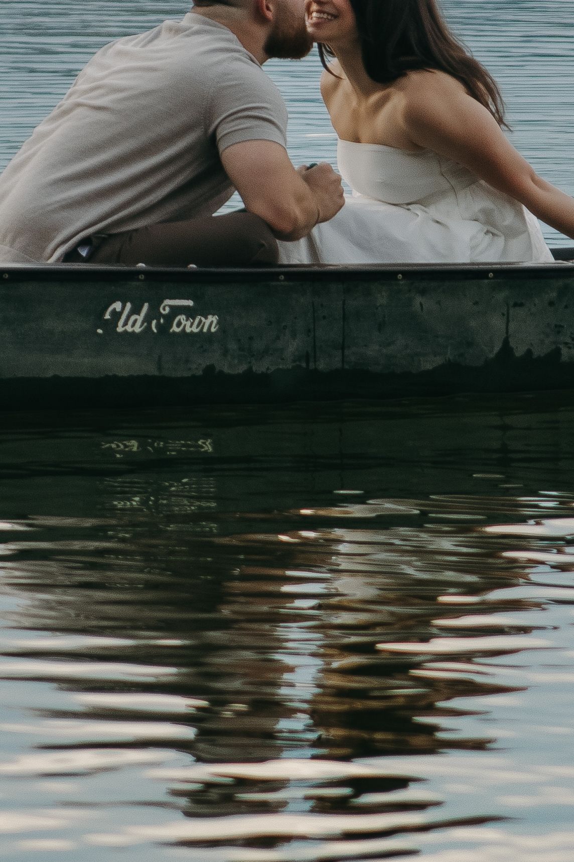 A romantic couple sits at the edge of a dock over calm rippling water on a peaceful afternoon.