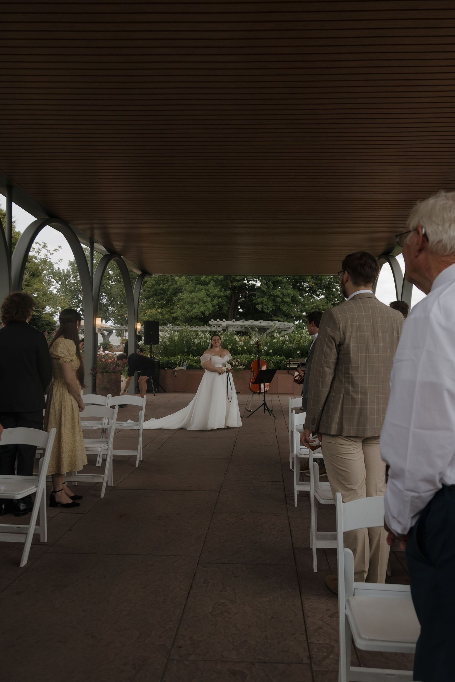Wedding ceremony under an elegant pavilion with bride in white gown standing at the altar before seated guests.