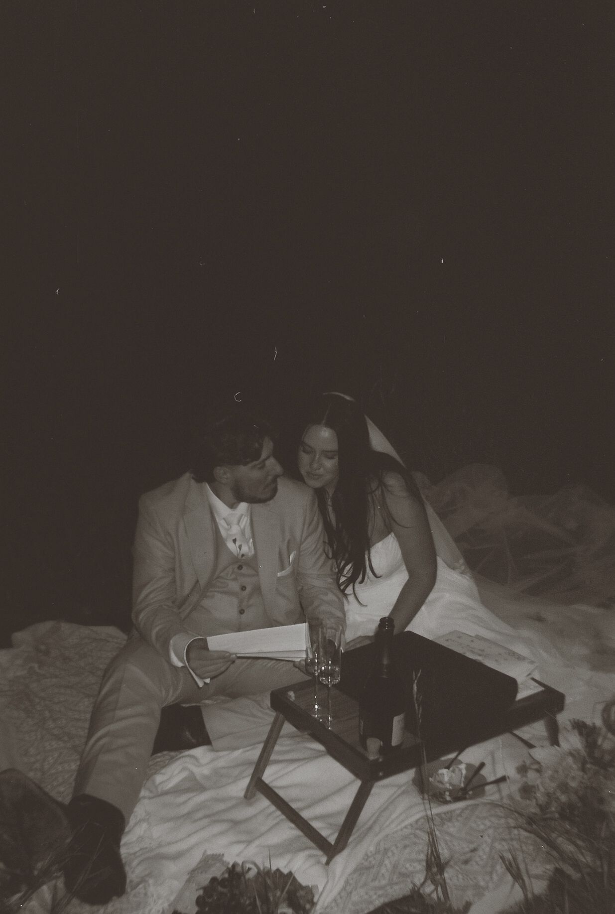 Black and white romantic photo of bride and groom sharing an intimate picnic moment together at night.