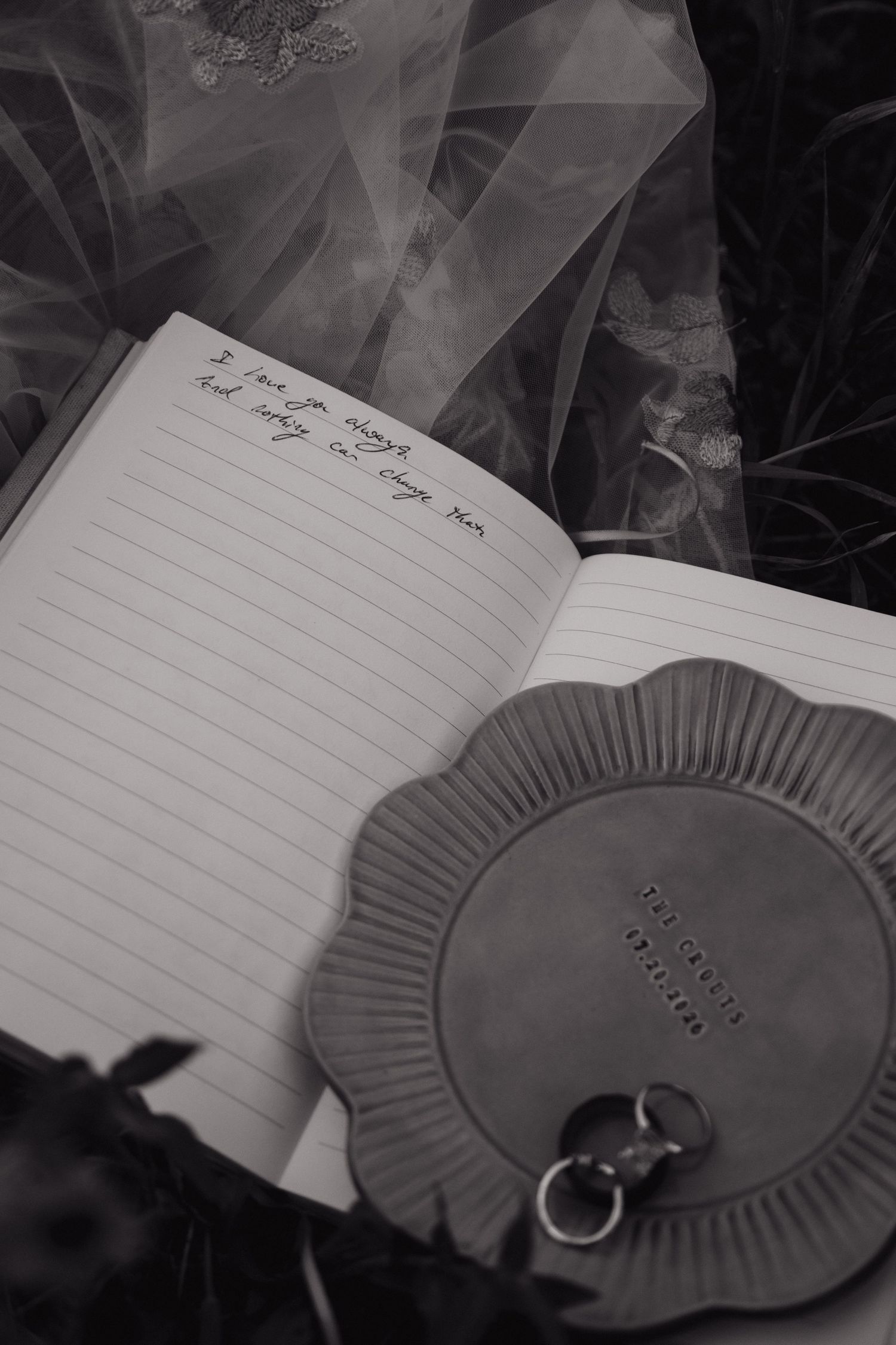 Black and white photo of handwritten wedding vows in a journal beside a ring dish with wedding bands.