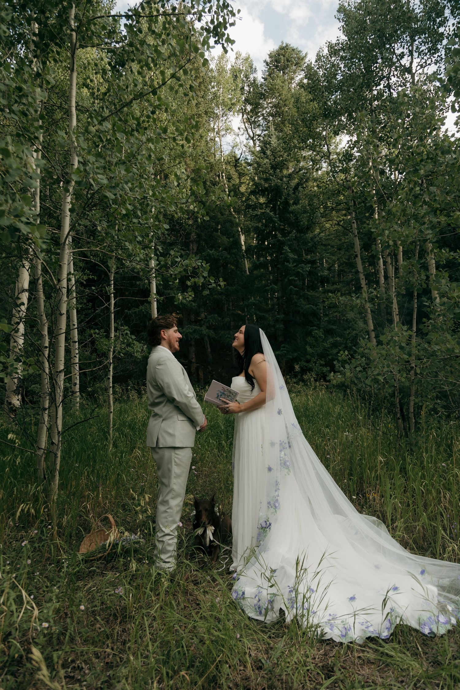 Bride and groom exchange vows in a lush forest clearing, bride wearing floral embroidered veil and gown.