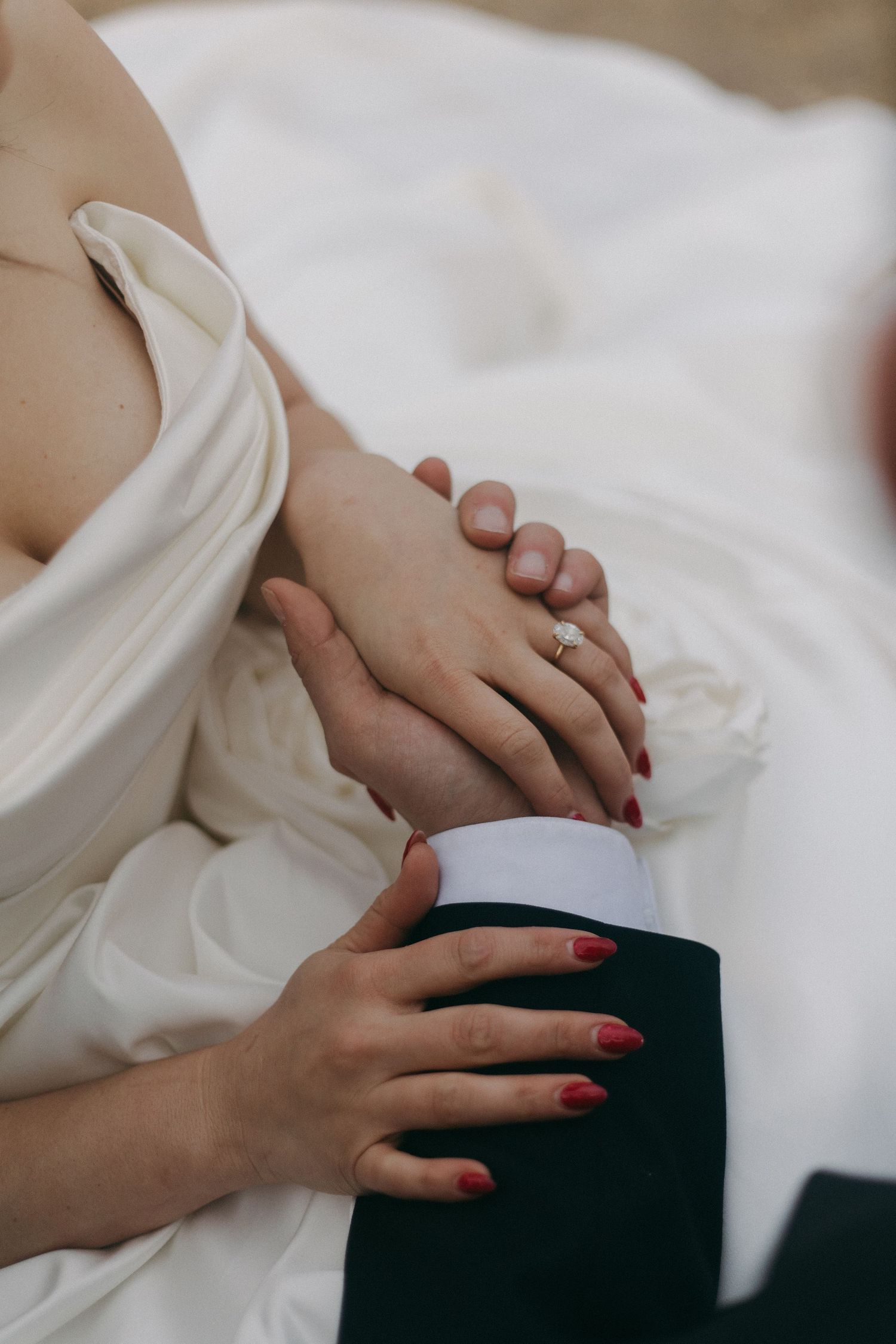 Close-up of hands with red nails and wedding ring resting on formal attire.