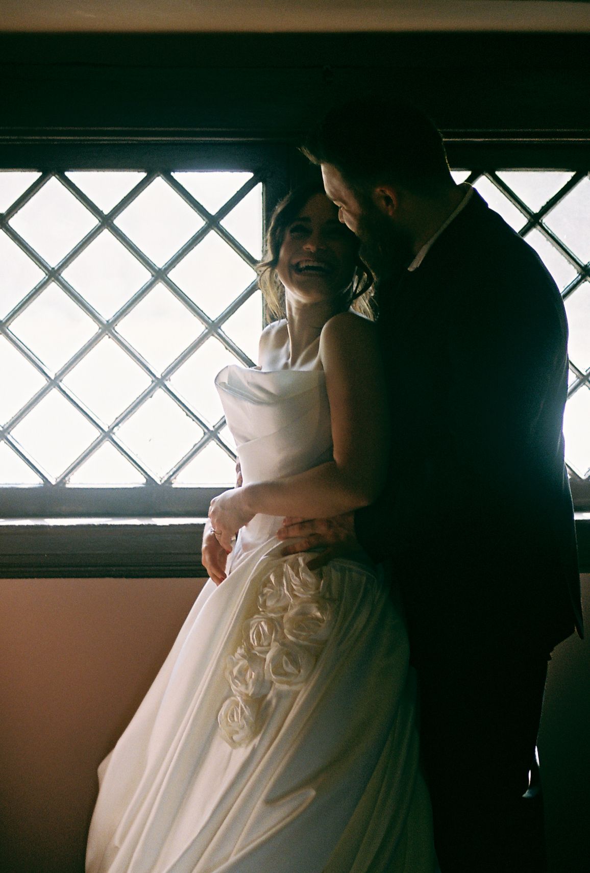 Dramatic lighting through latticed windows illuminates details of a white wedding gown.