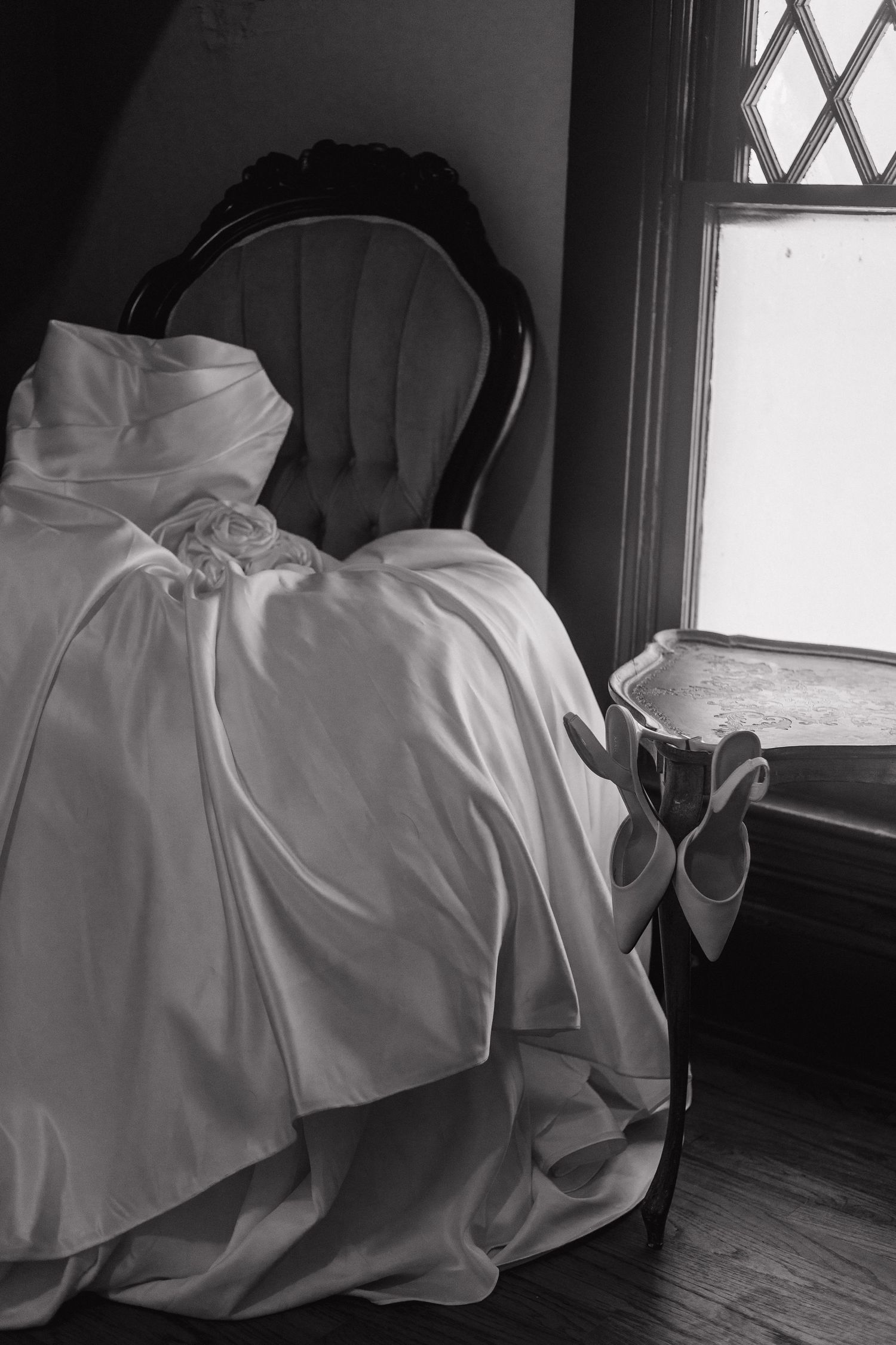 A white wedding dress flows gracefully across dark hardwood flooring near a window.