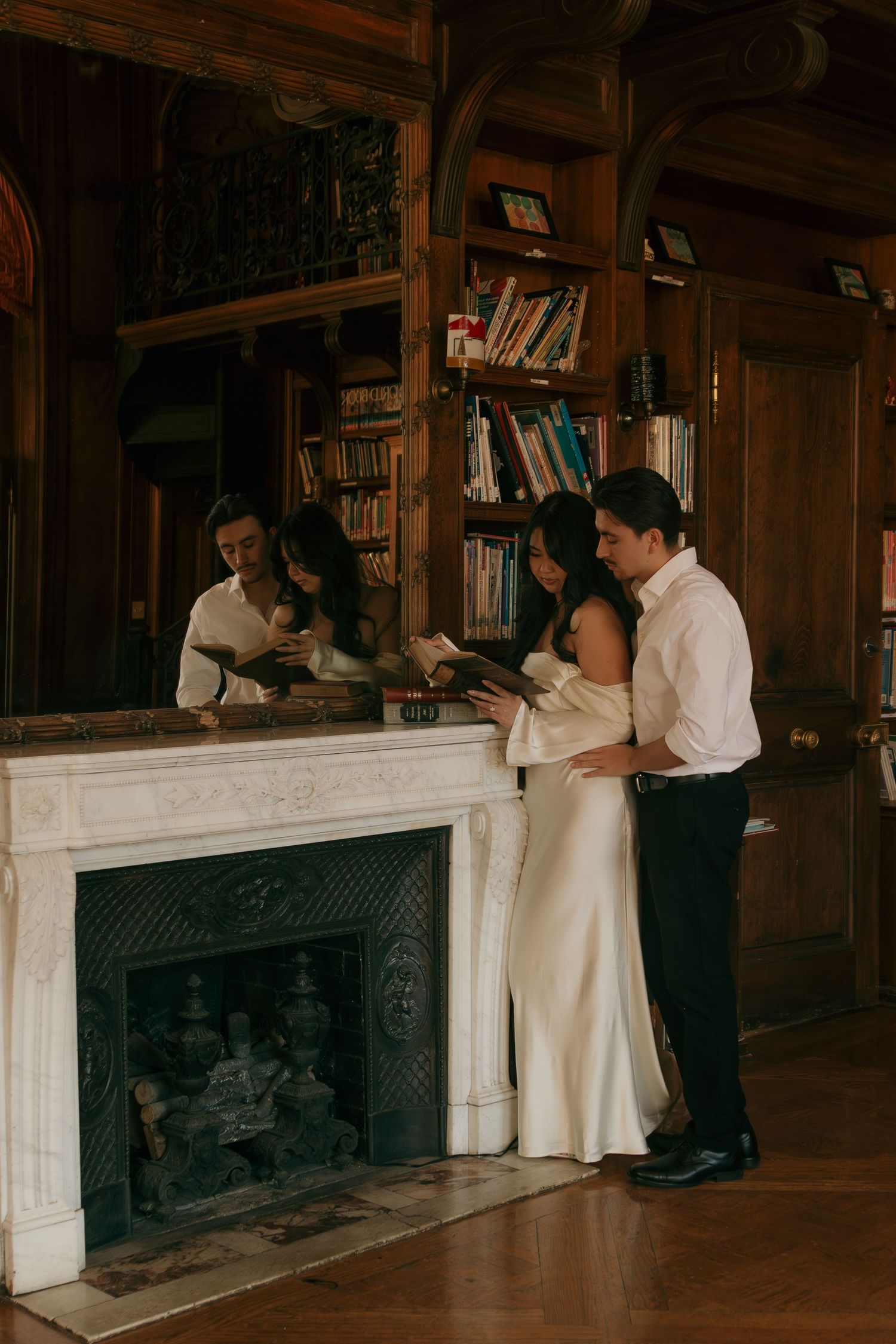 A romantic couple embraces near an ornate fireplace mantel in a library setting.