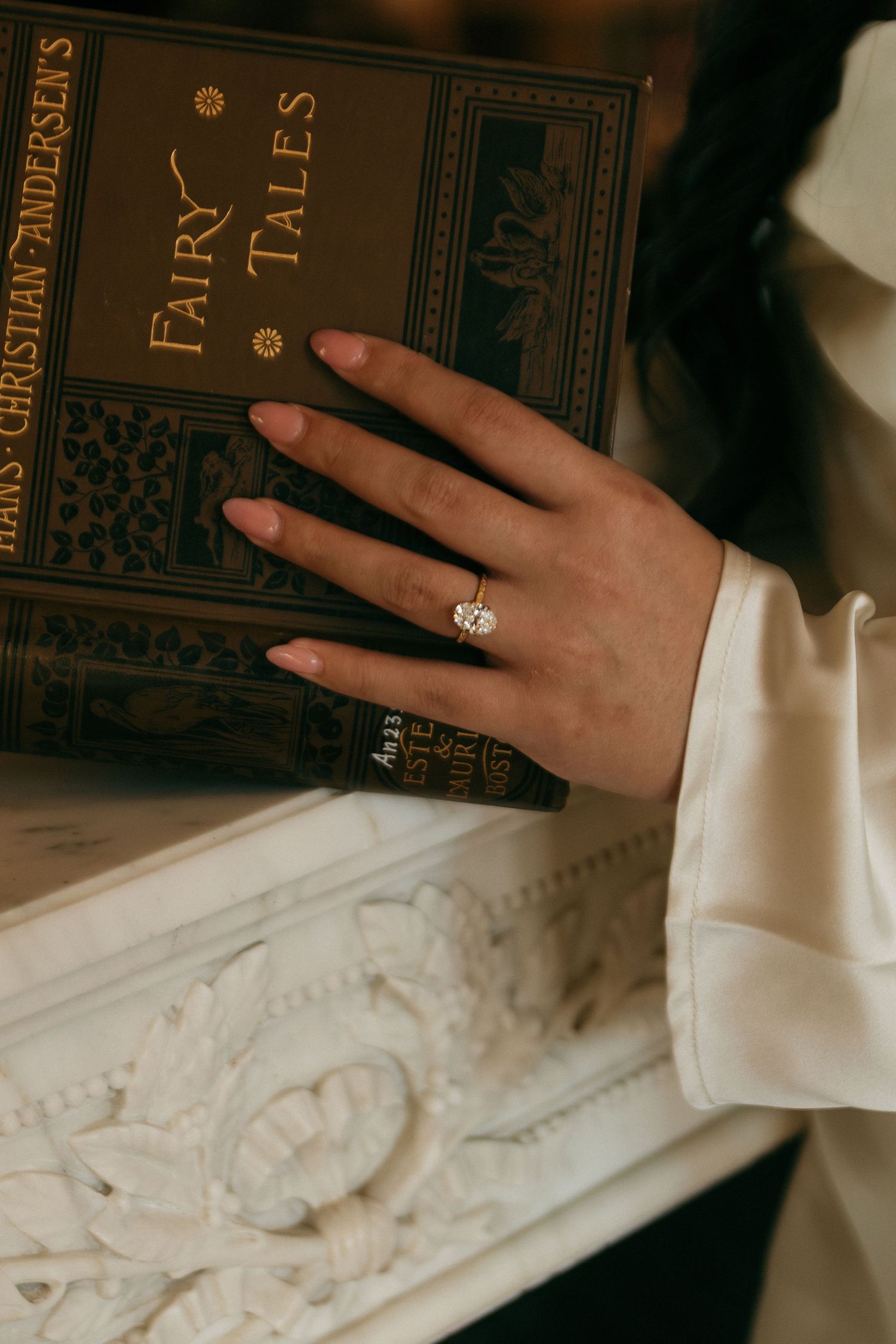 Hands reaching for vintage books with dark covers on an ornate white shelf.